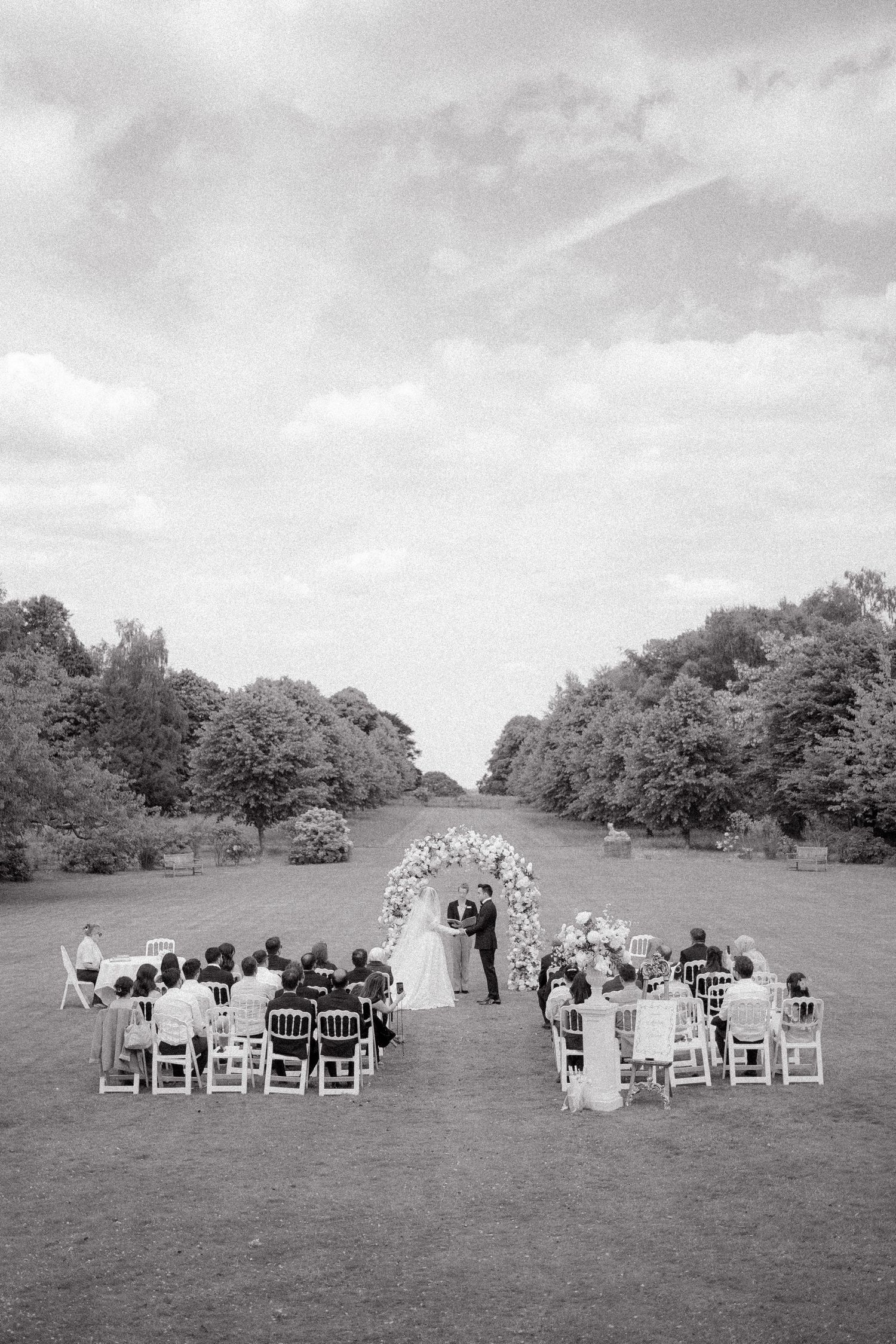 White chairs arranged on a grassy hillside for an outdoor wedding ceremony with trees in the background.