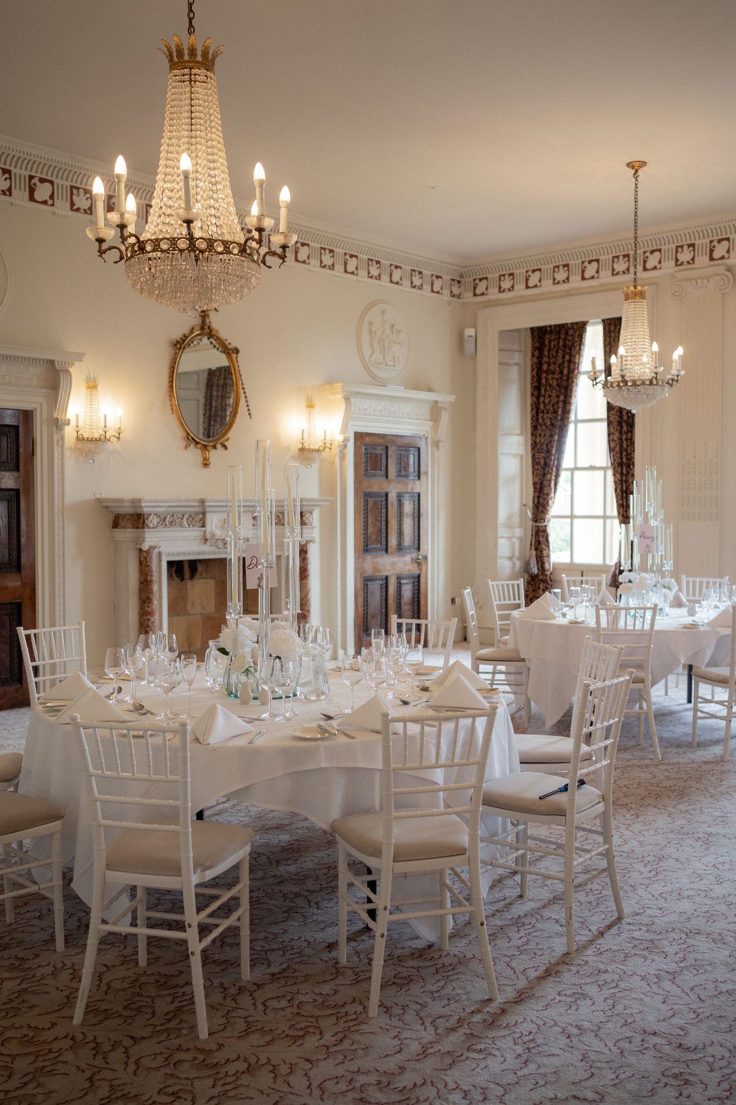 Formal dining room set with white chairs and crystal chandeliers in a classic ballroom setting.