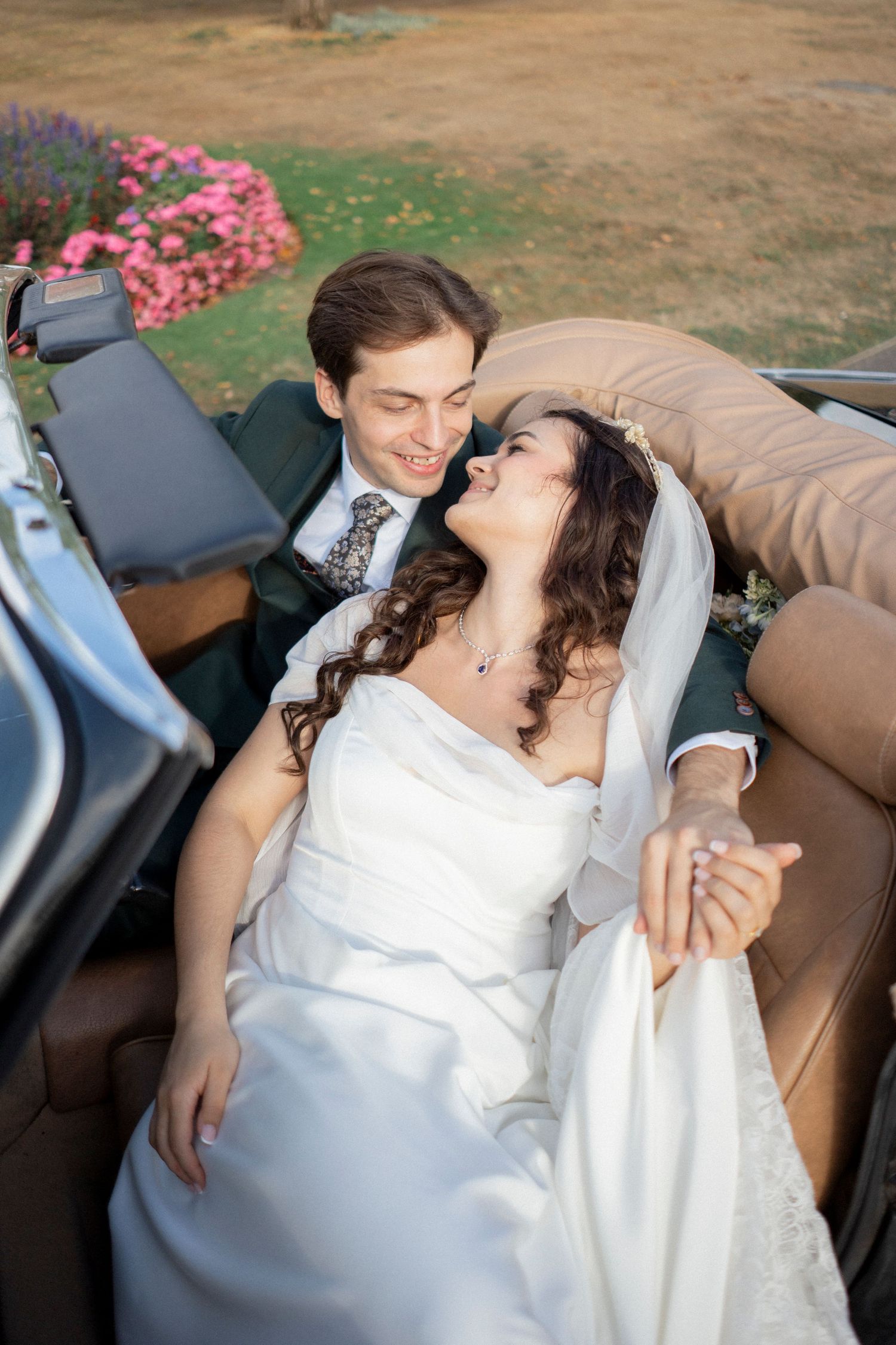Bride and groom share a romantic moment in a vintage convertible car on their wedding day.