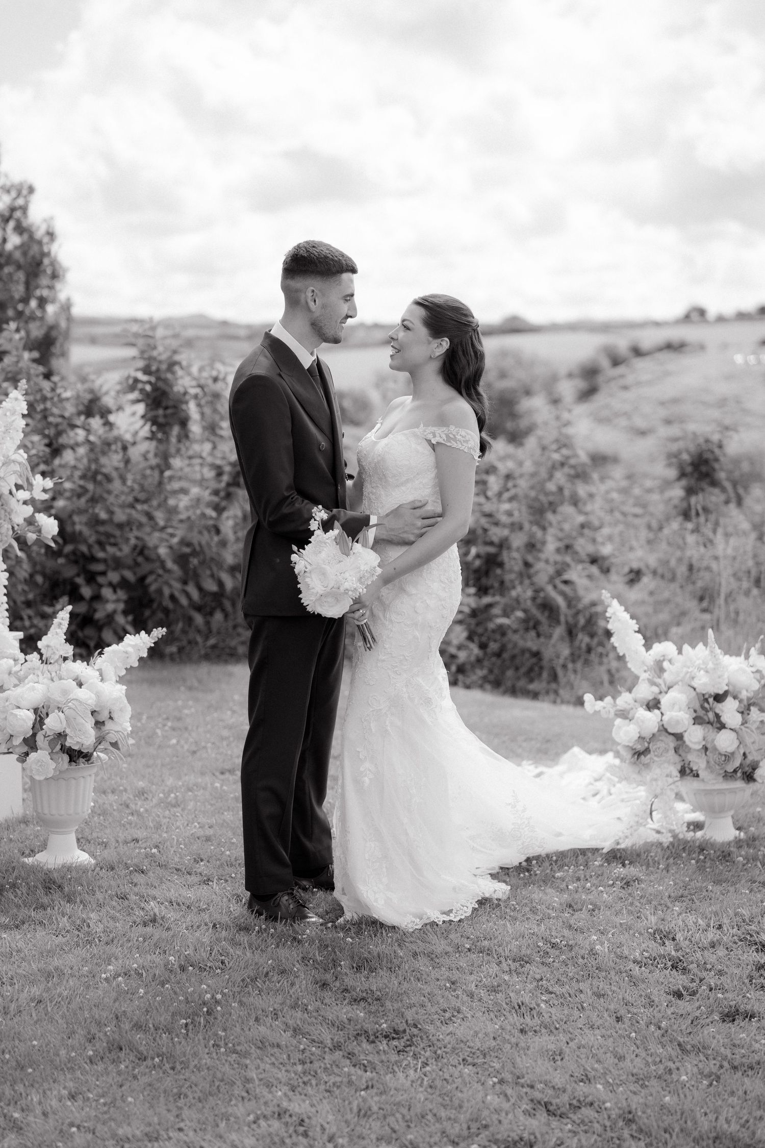 Black and white portrait of newlyweds with elegant white floral arrangements in the background.