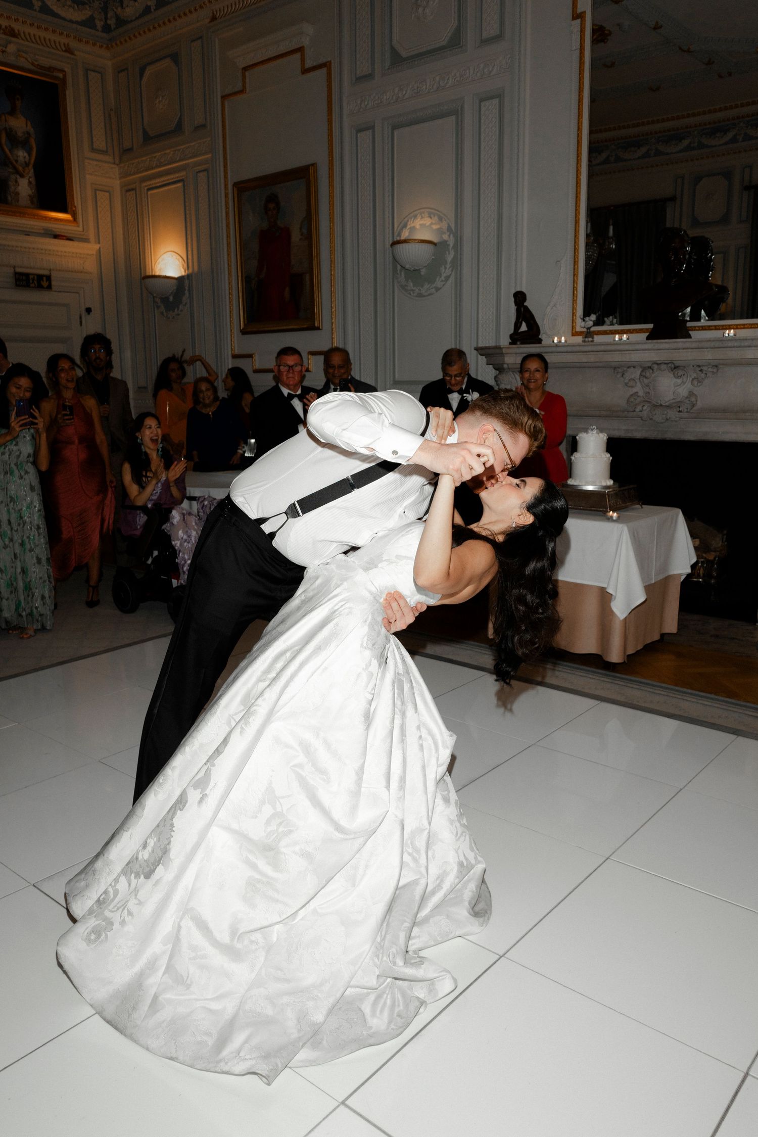 Bride and groom share a romantic dip kiss on white dance floor at elegant wedding reception.