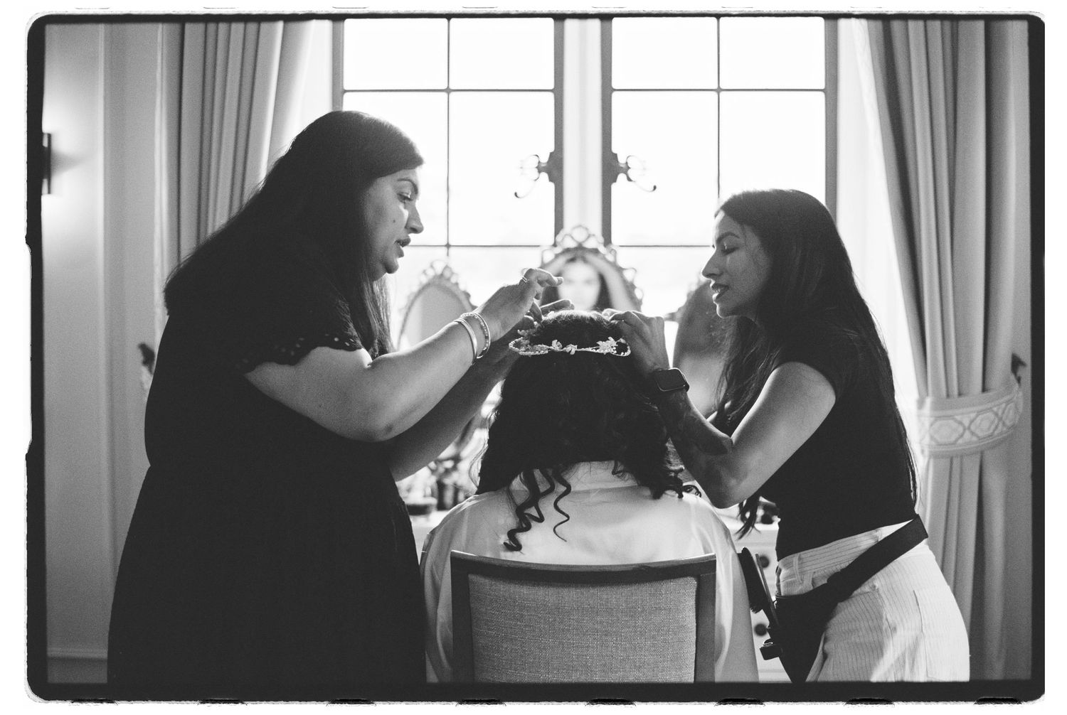 Two women share a joyful moment over a decorated cake in a bright room, captured in black and white photography.