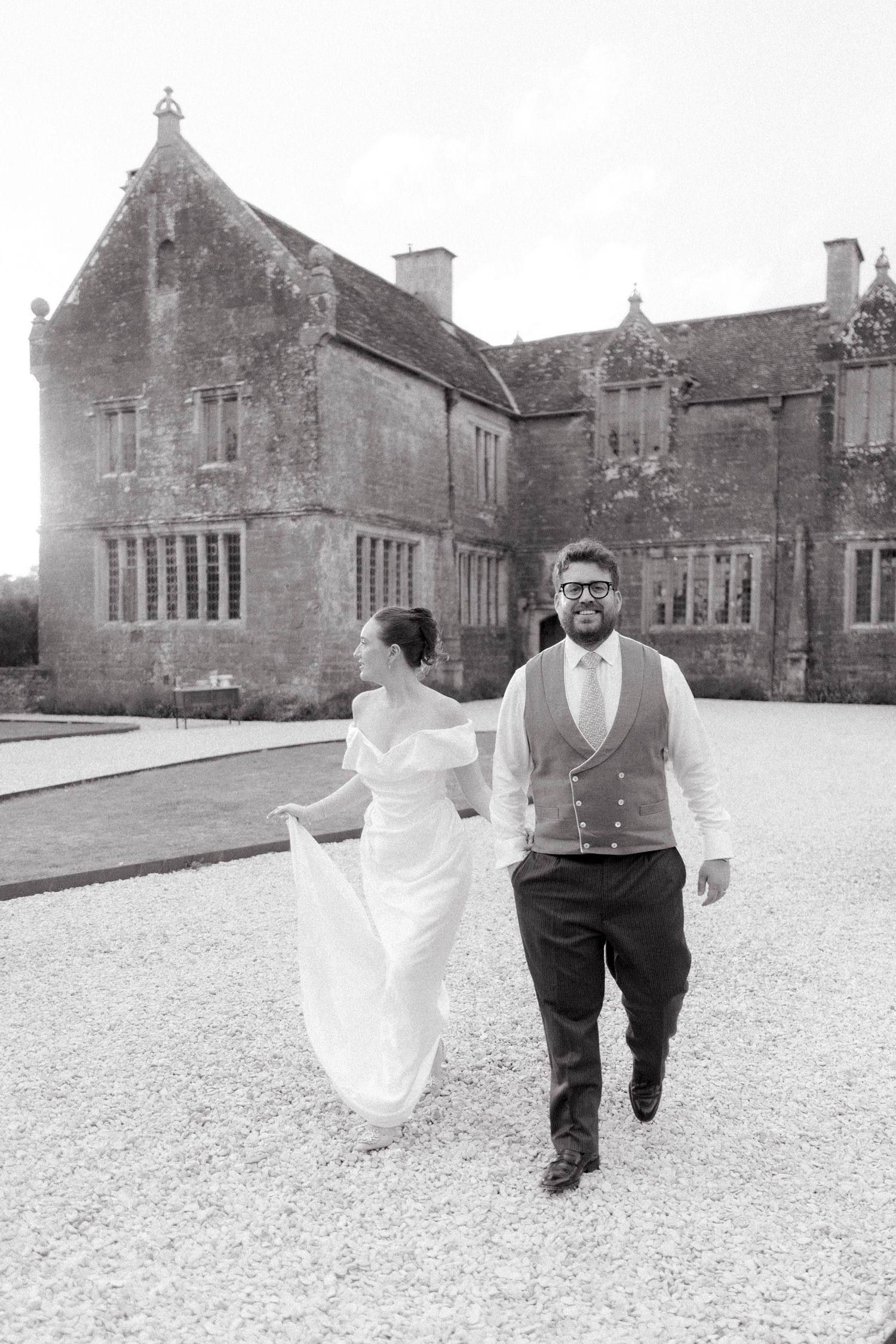 Bride and groom walk hand in hand outside a historic manor house.
