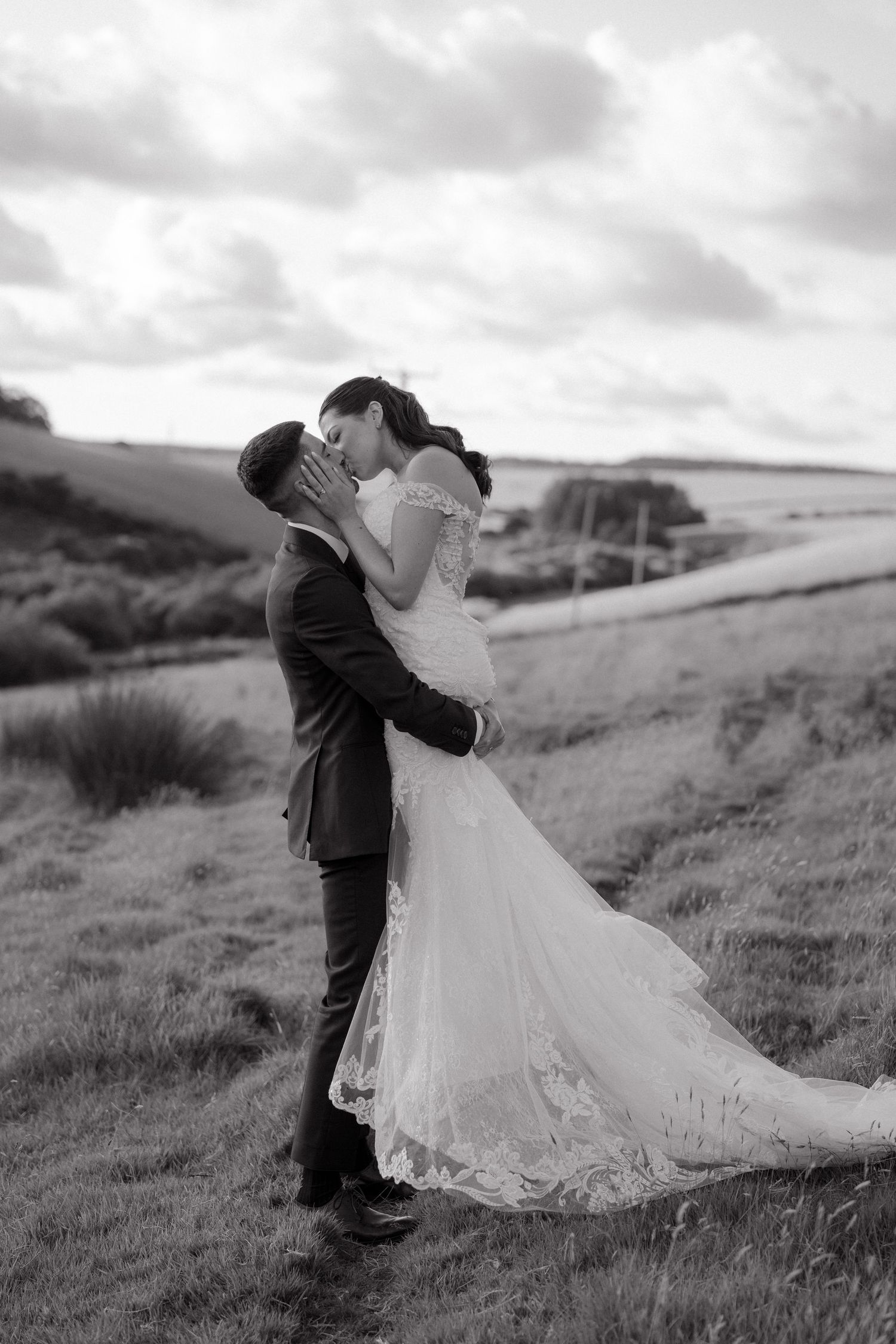 A romantic black and white wedding portrait of a couple embracing on a hillside.
