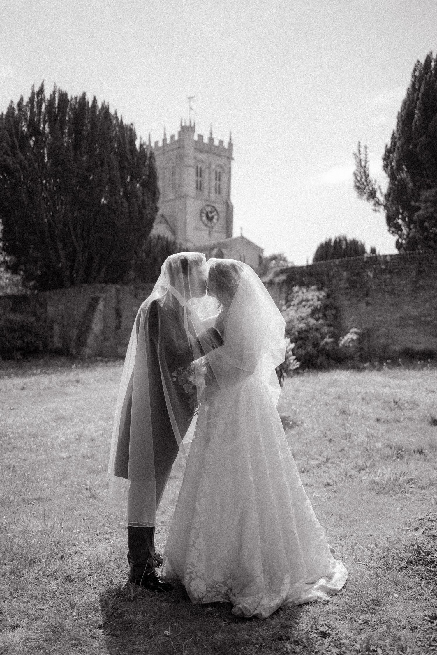 A series of black and white wedding photos showing a couple walking away through a grassy field near a church.