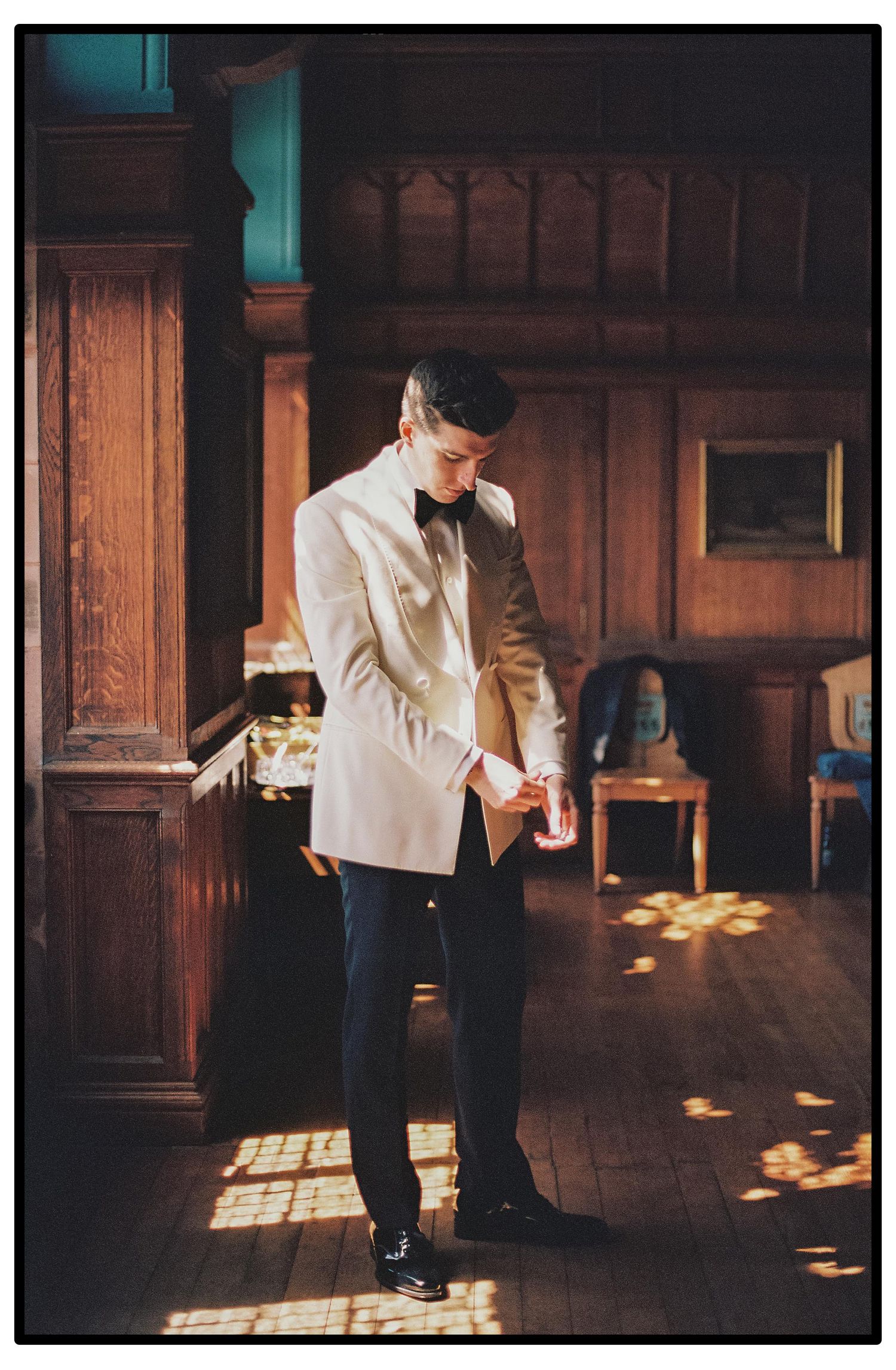 A person in a white shirt and dark pants dances across a sunlit wooden floor in an elegant interior space.
