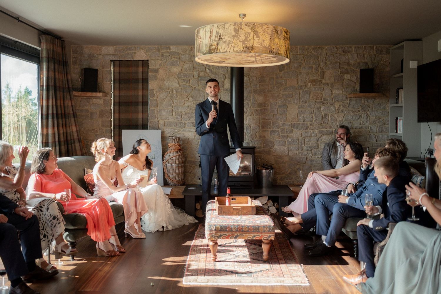 Wedding guests gathered in a rustic room listening to a speech during the reception.