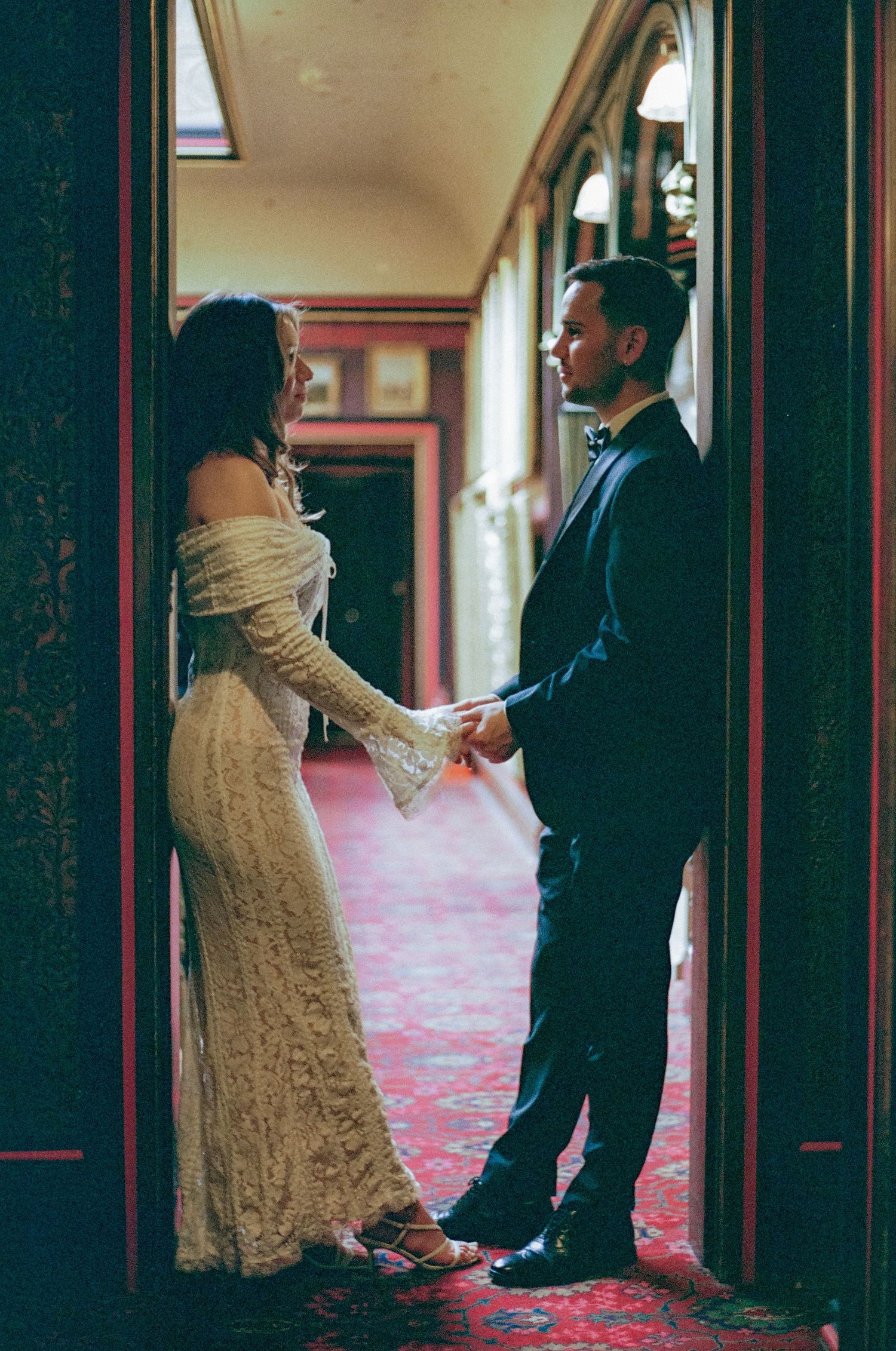 Couple in formal attire dancing in ornate hallway with red carpet.