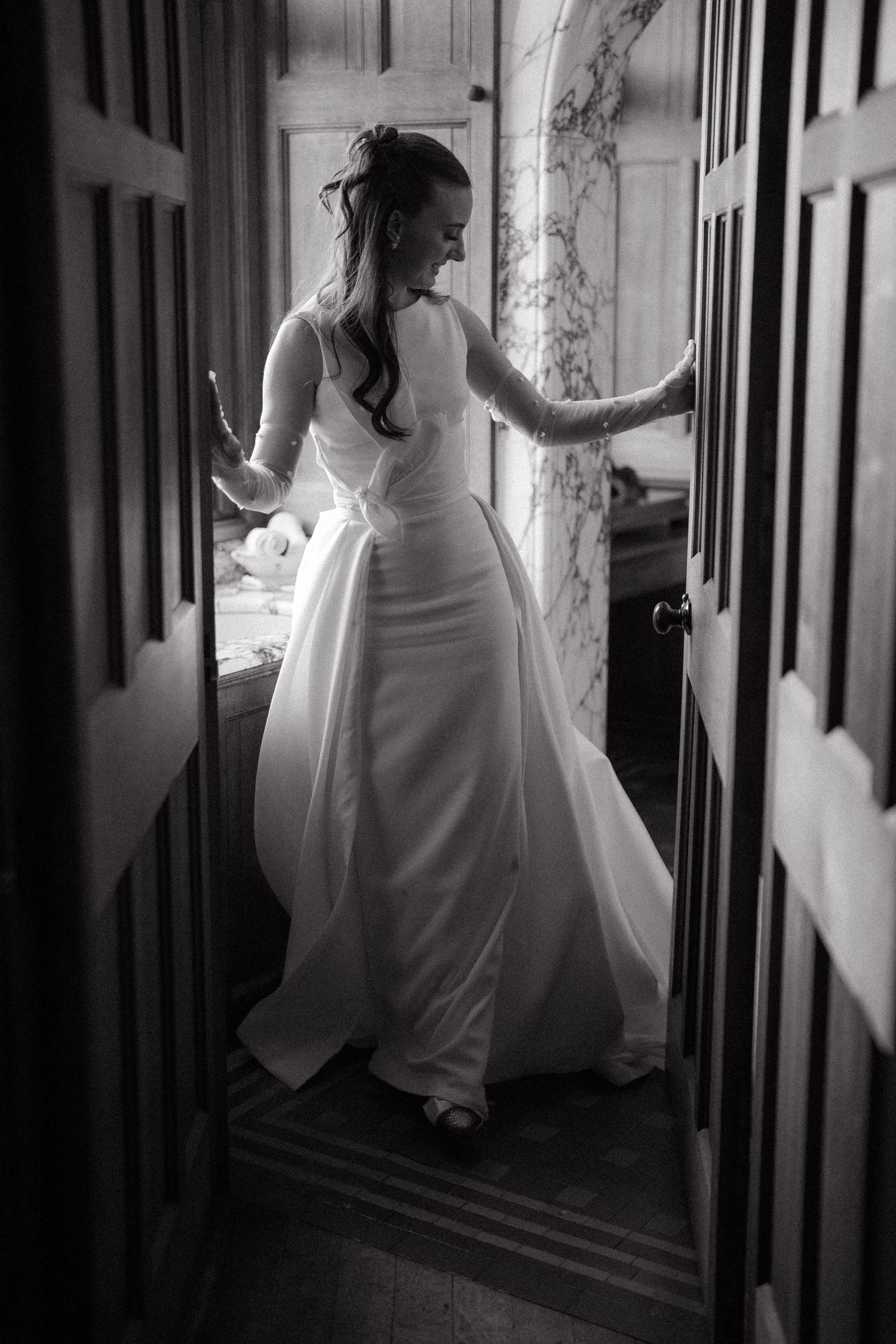Artistic black and white photo of a bride walking through a dimly lit hallway.