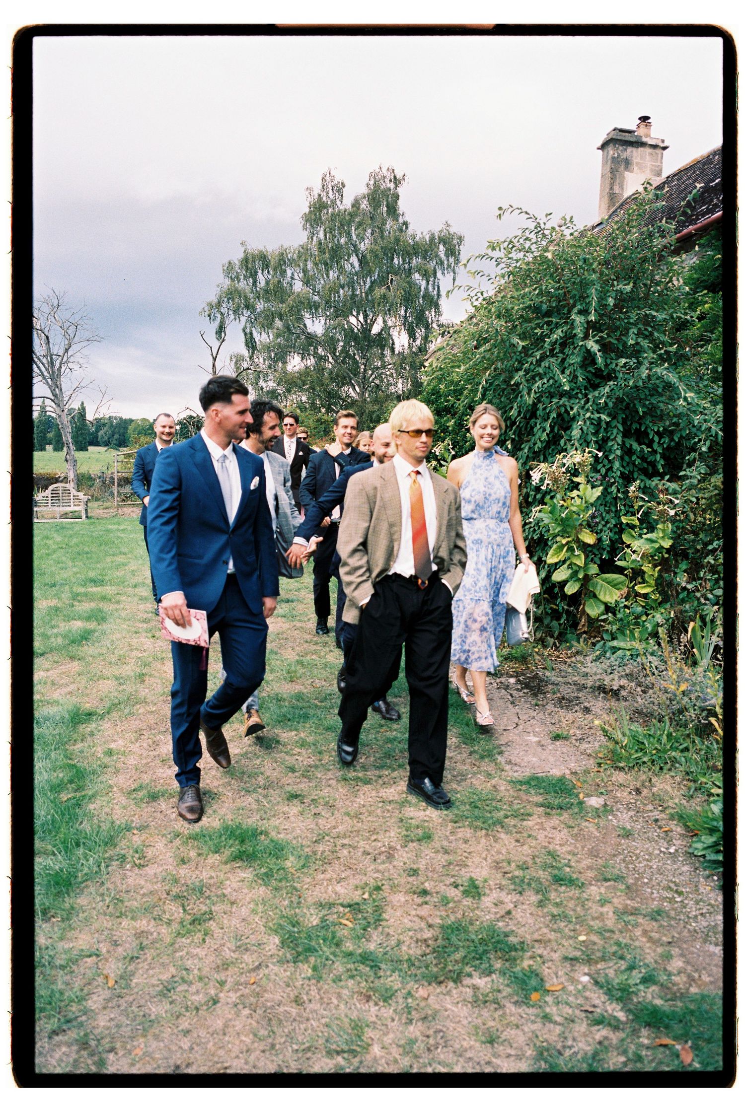 Wedding guests stroll across garden grounds following outdoor countryside ceremony.