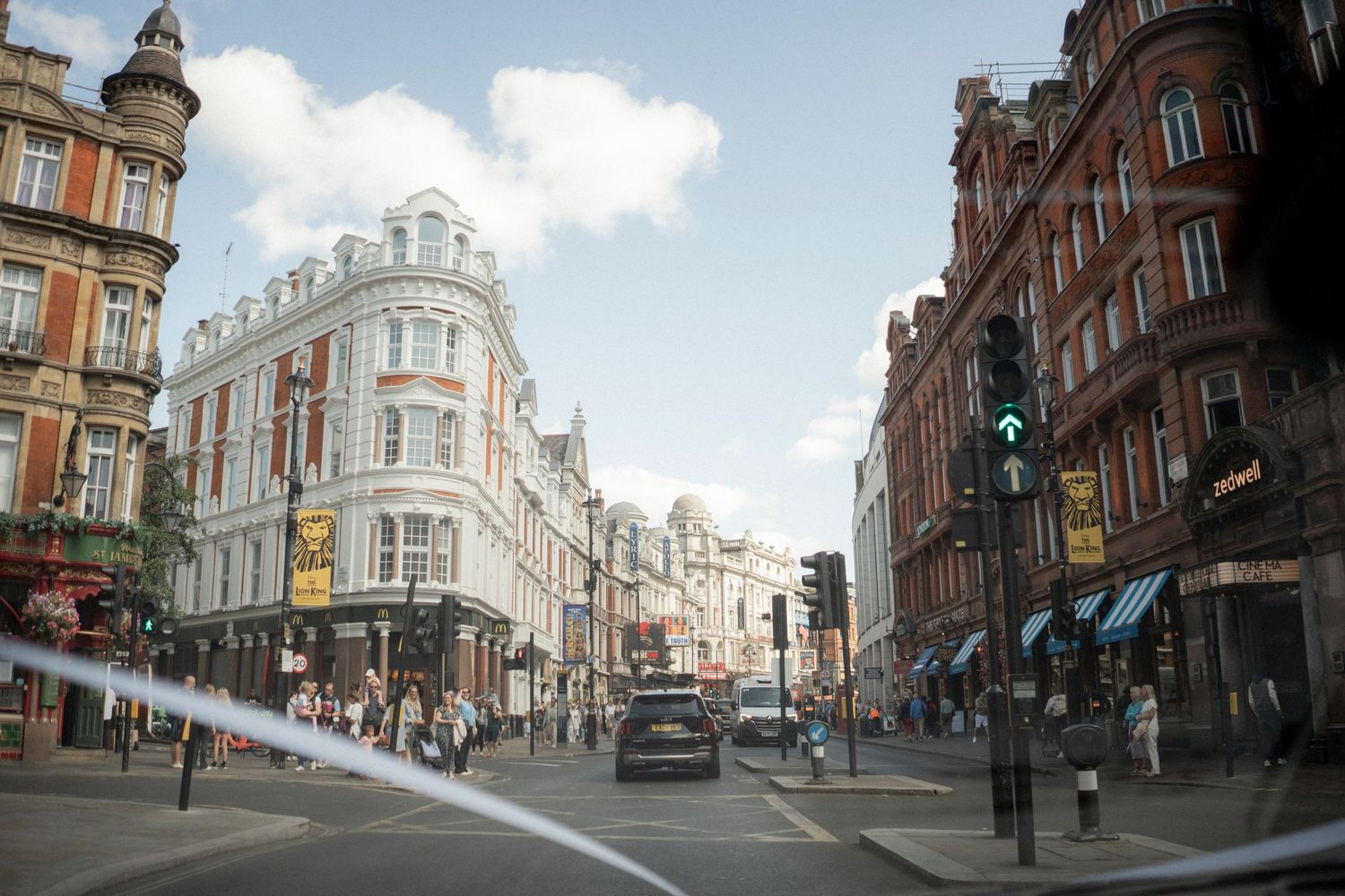 Busy London street intersection with historic red brick buildings, traffic lights, and pedestrians on a sunny day.