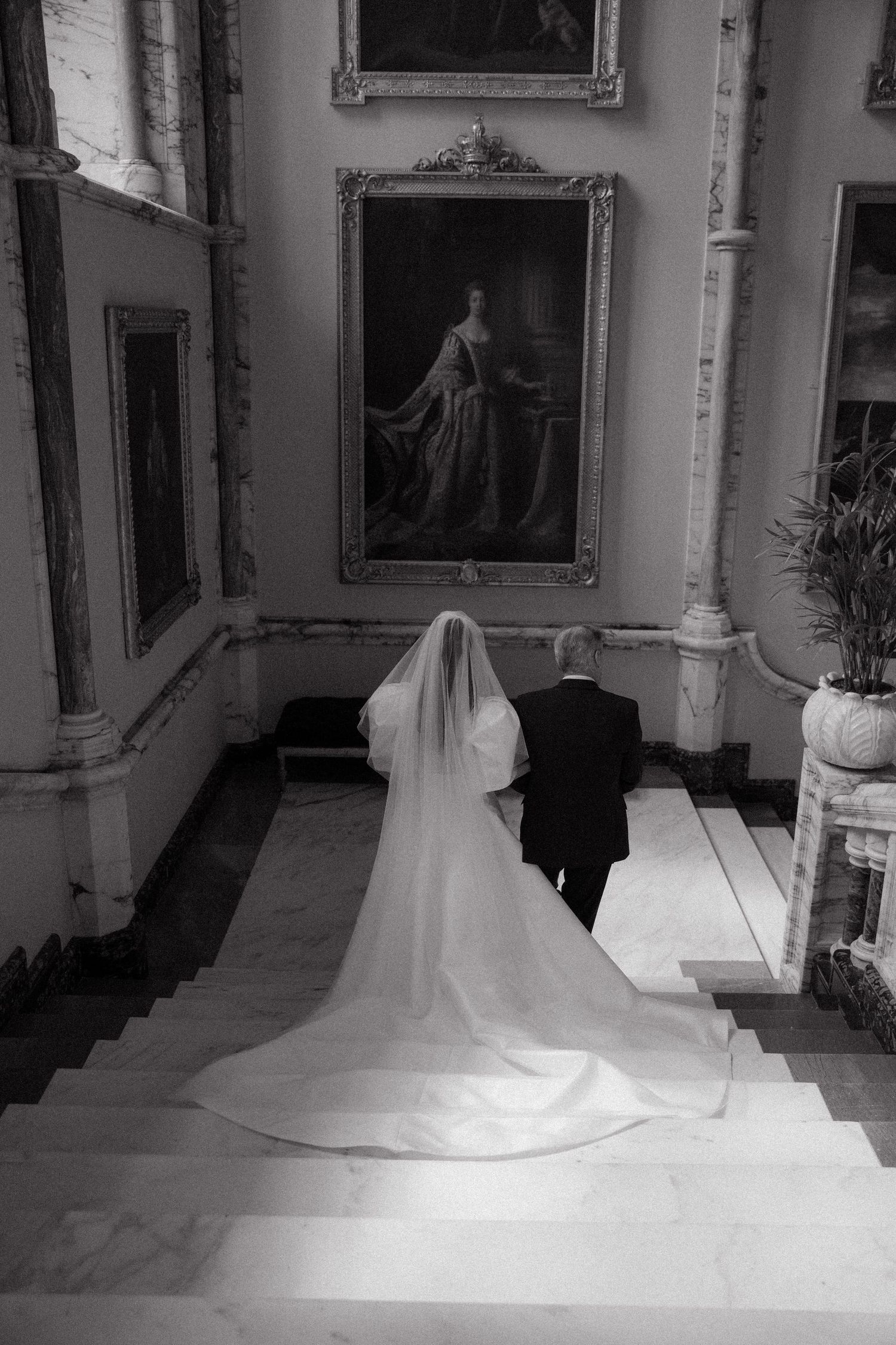 Wedding dress train flowing down grand staircase in historic interior hallway.
