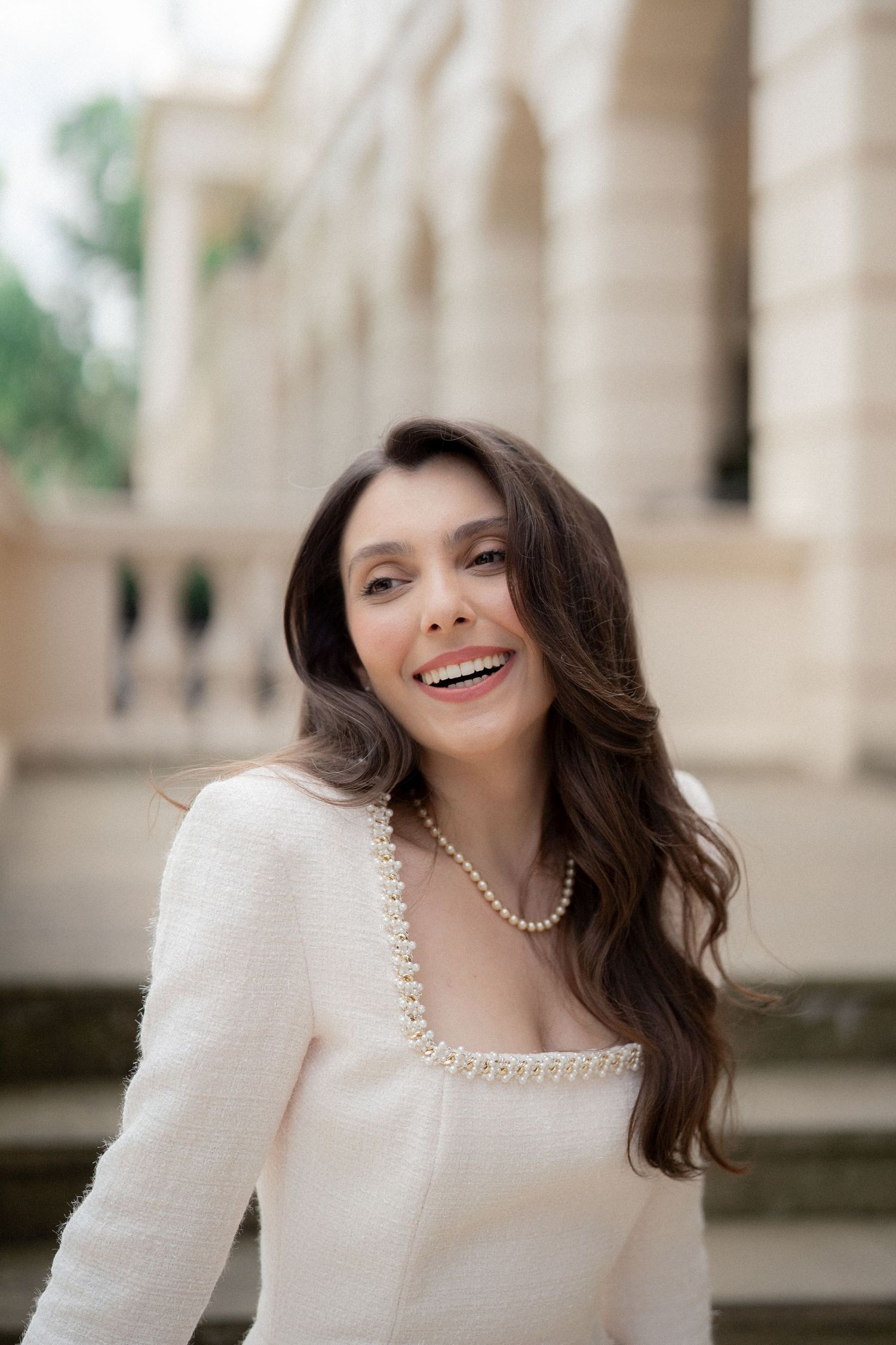 Person in a white dress poses joyfully against a classical building backdrop.