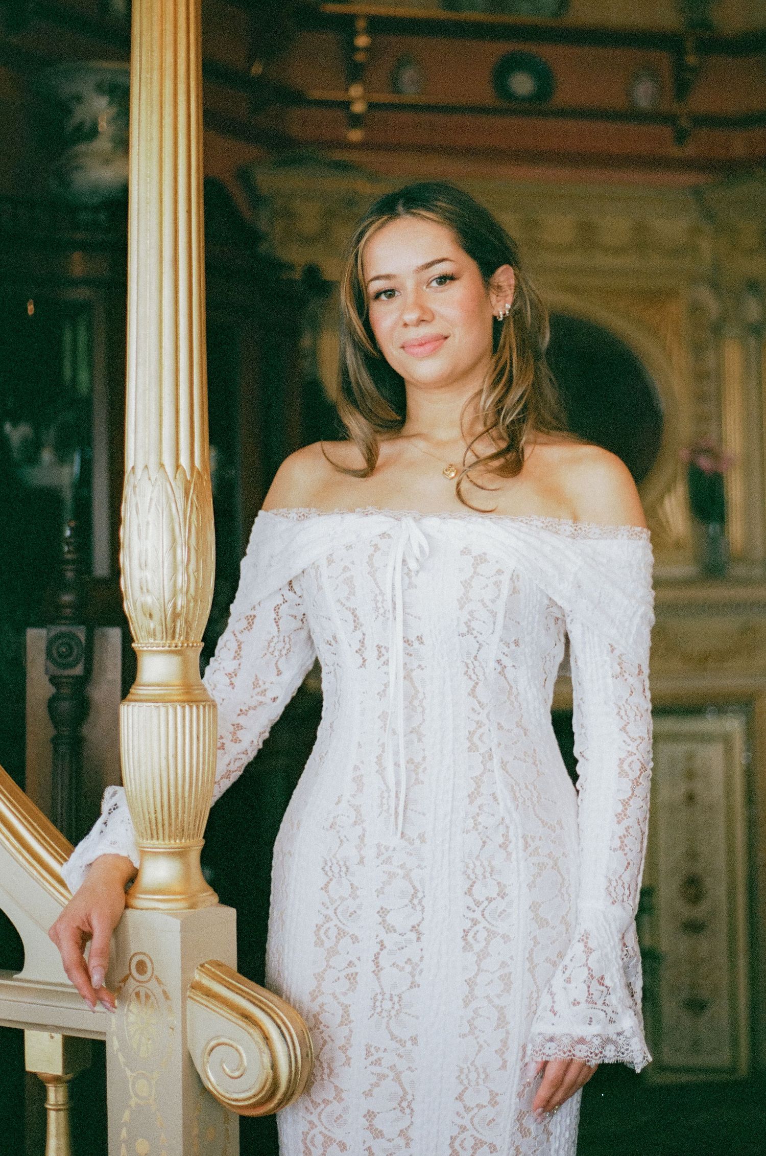 Bride poses in an ornate off-shoulder lace wedding gown next to decorative columns.