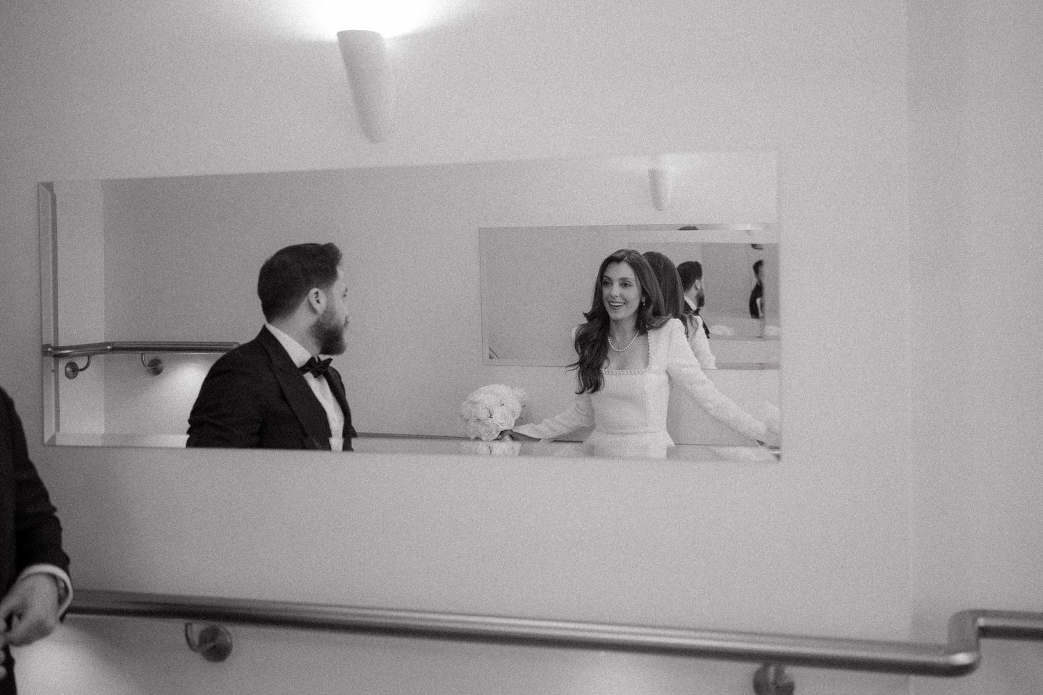 Black and white wedding photo of bride and groom reflected in a mirror, sharing a tender moment.