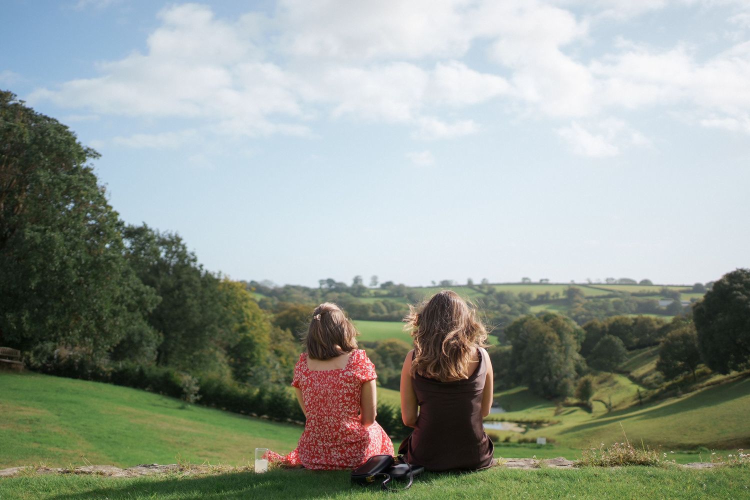 People sitting on a hillside overlooking a scenic valley with rolling green hills and trees in the countryside.