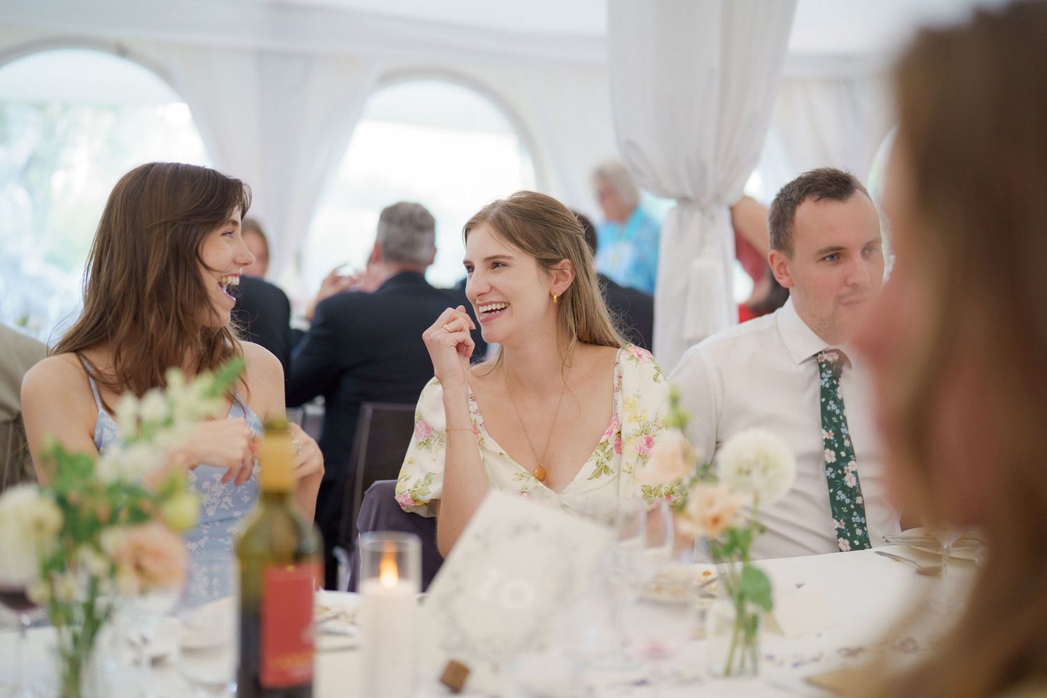 Wedding guests enjoy a lively conversation during an elegant reception dinner at a white-tablecloth venue.