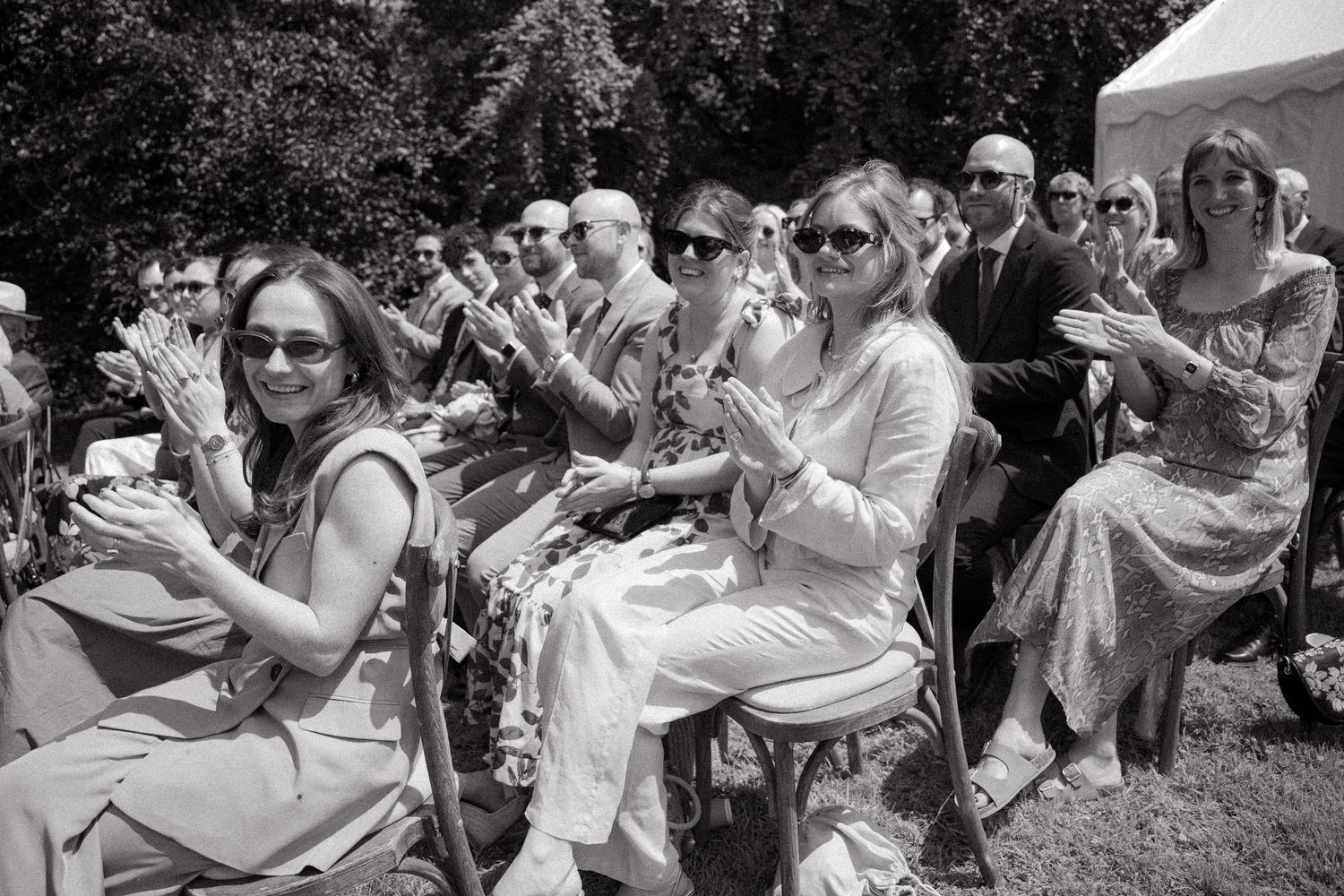 A black and white photo strip showing candid moments of people laughing and embracing at an outdoor gathering.