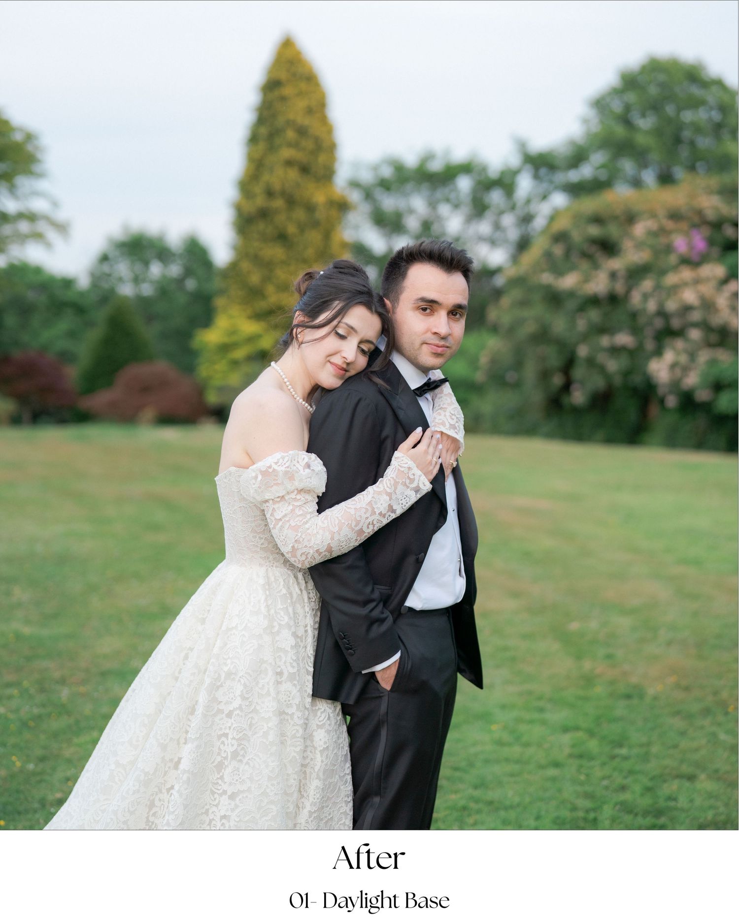 A couple in formal wedding attire embraces on a green lawn with trees in the background.
