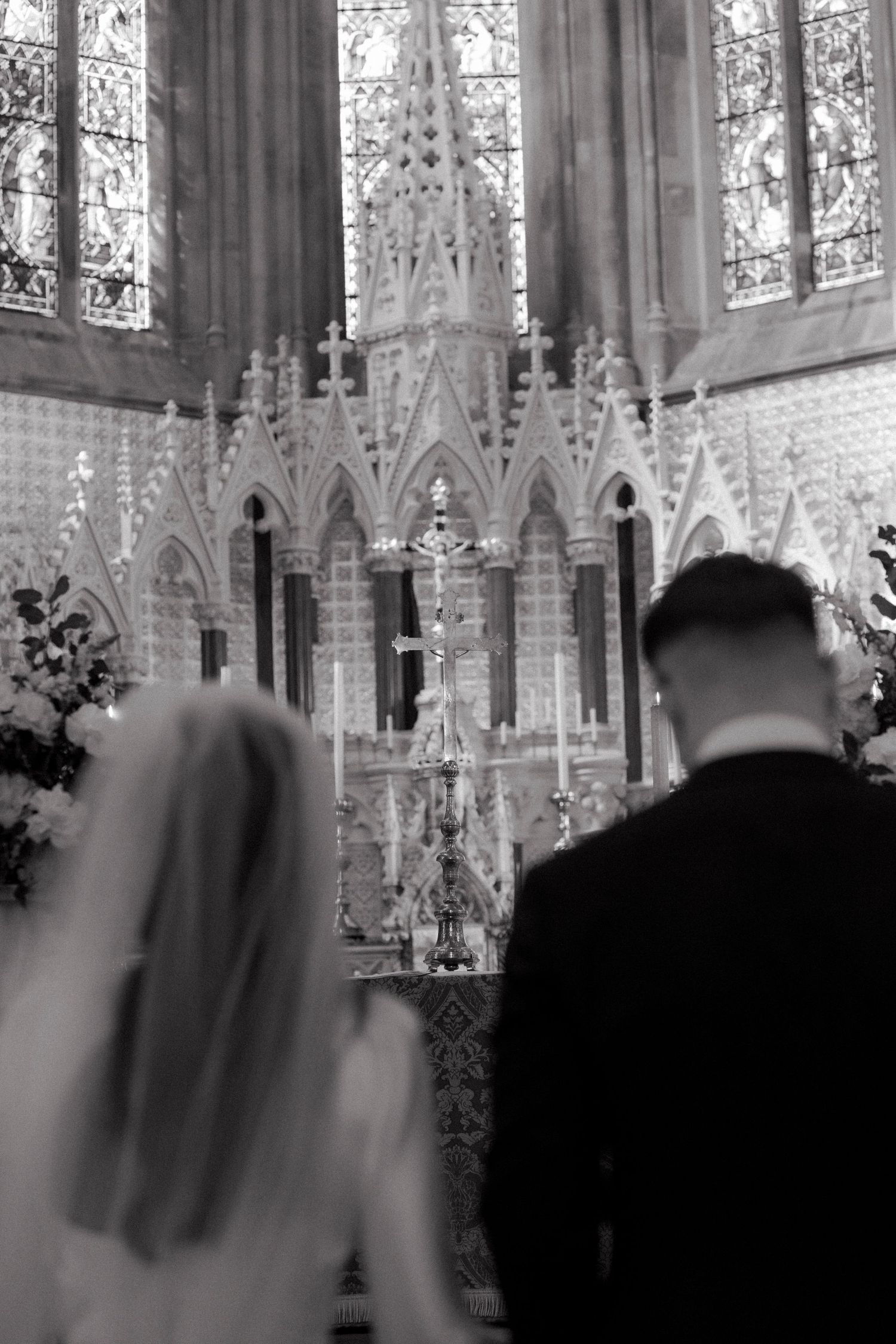 Black and white photo of bride and groom at ornate church altar during wedding ceremony.