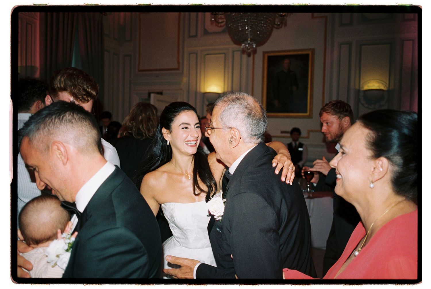Bride in strapless white gown smiling with elderly gentleman at elegant wedding reception in formal venue.