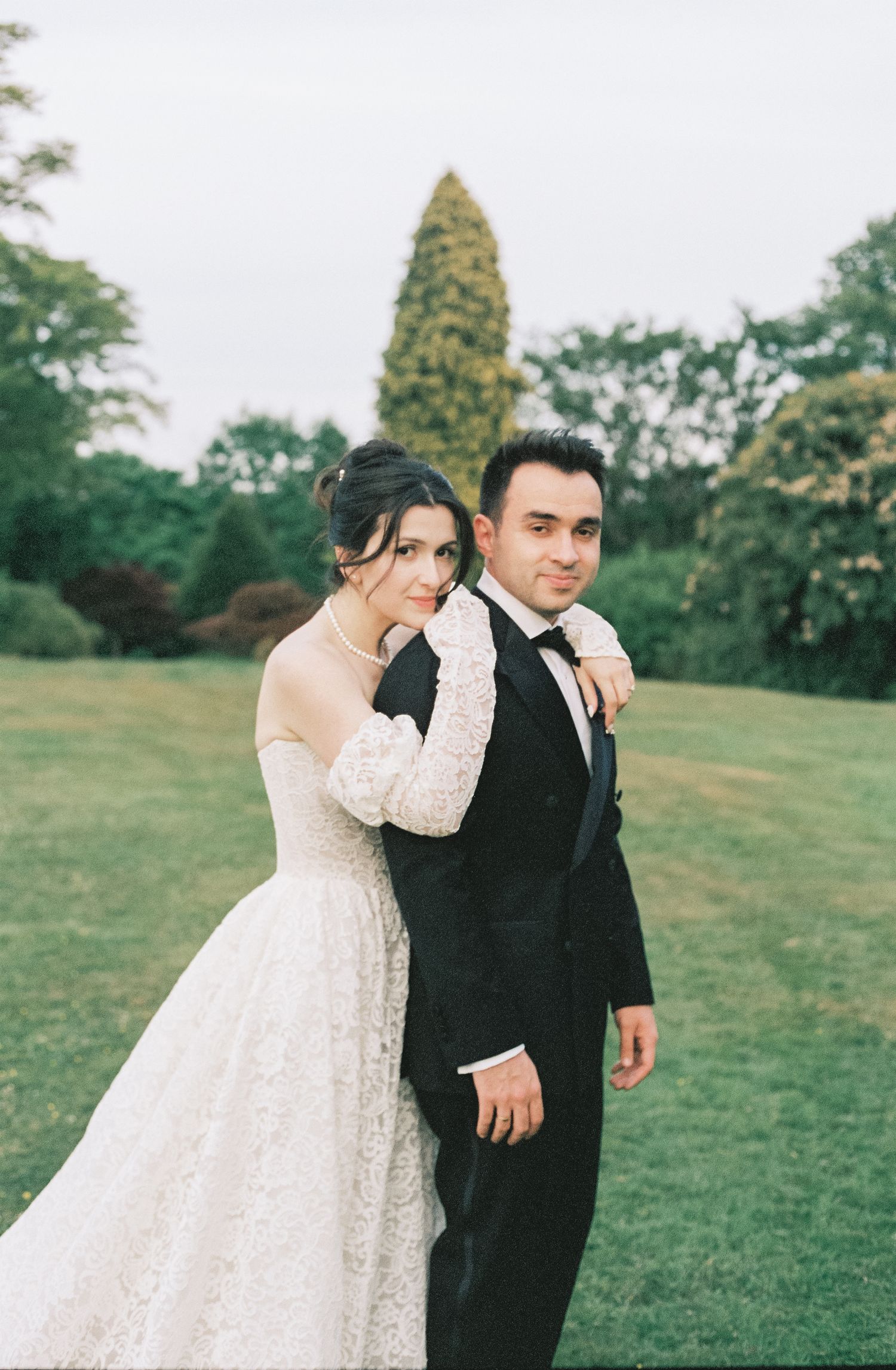 A couple in wedding attire share a tender moment while walking together on a grassy field.