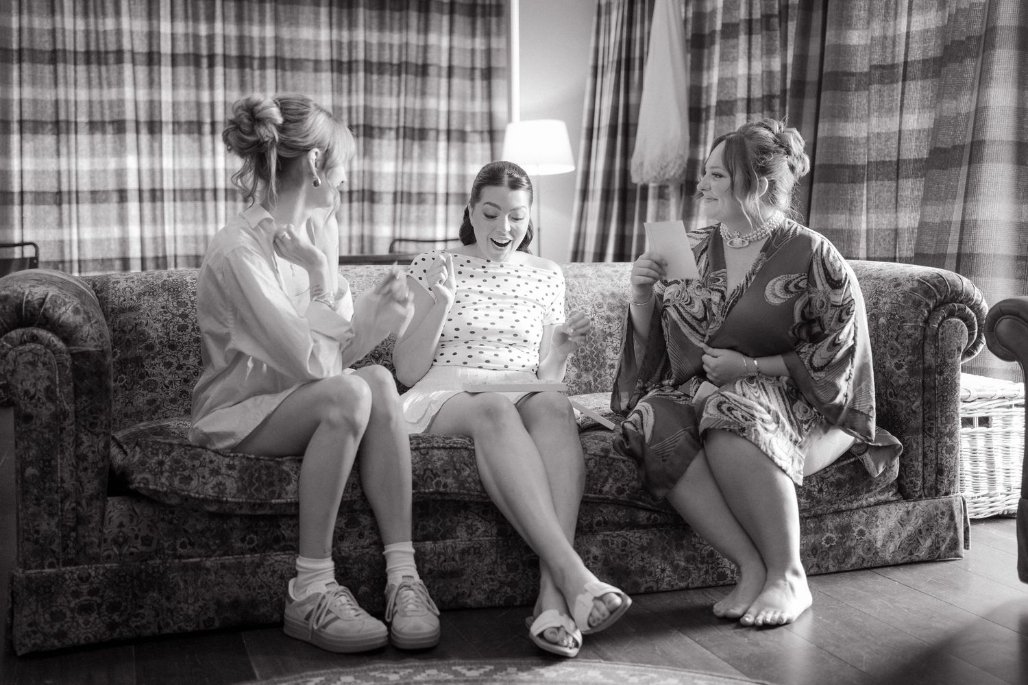 Black and white image of wedding party members' feet in formal shoes sitting on a couch.