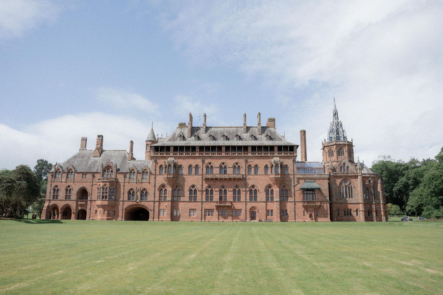 Panoramic view of a grand historic brick building with Gothic architecture set on a sprawling lawn.