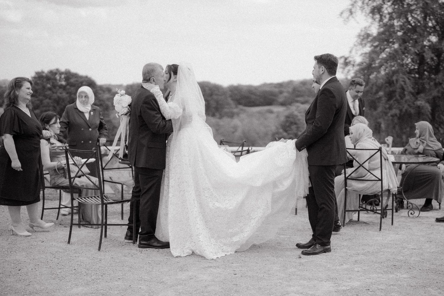 Wedding ceremony in progress with guests seated in black and white chairs on lawn.
