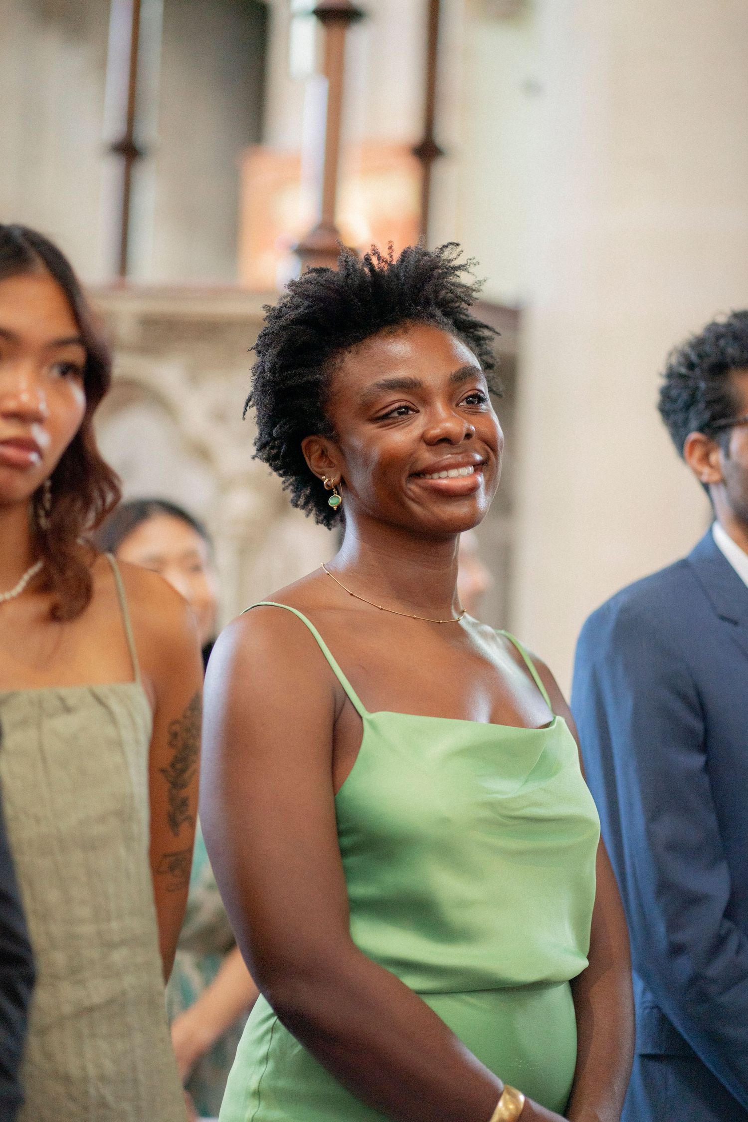 Smiling woman in green satin slip dress at a wedding ceremony inside a church.