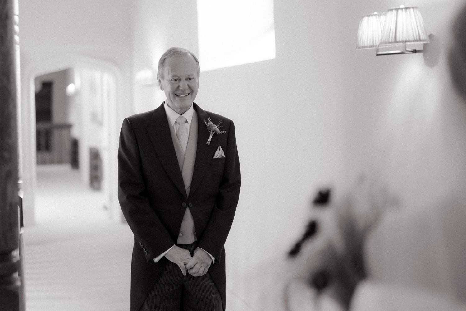 Emotional father of the bride smiling as he sees his daughter in her wedding dress during a black and white ceremony.