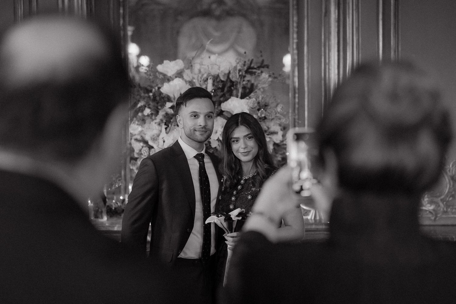 Couple posing for a photo at an elegant black and white event with floral decor in the background.
