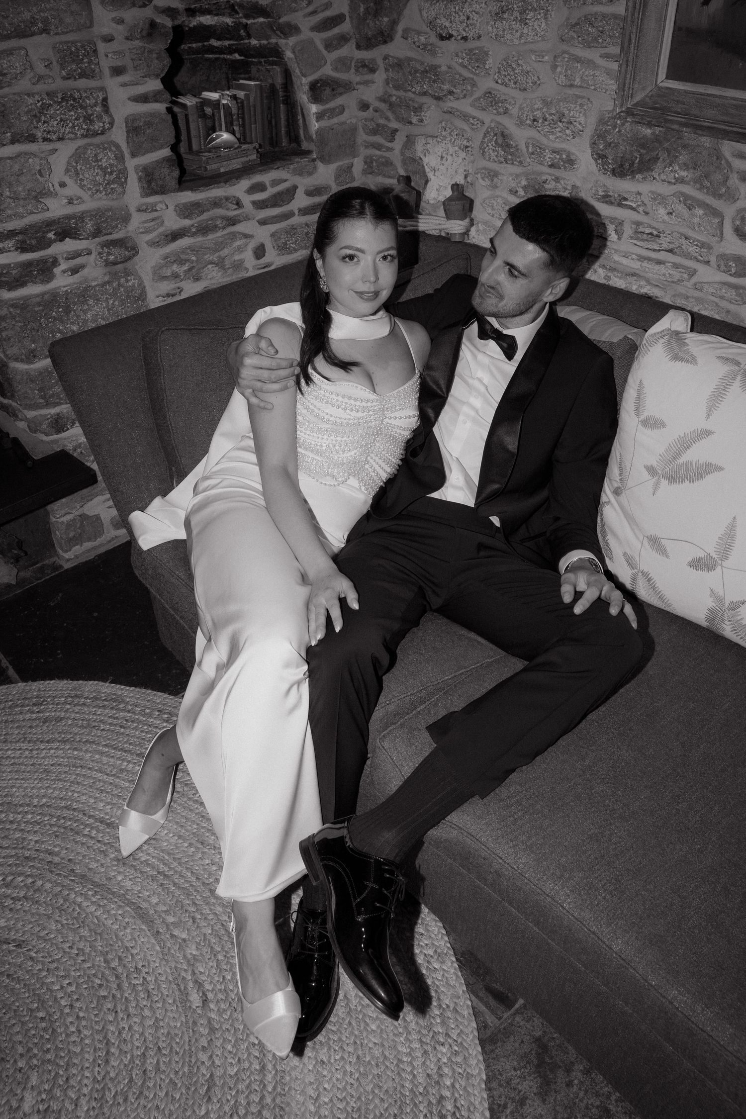 Wedding couple relaxing on a couch against a stone wall.