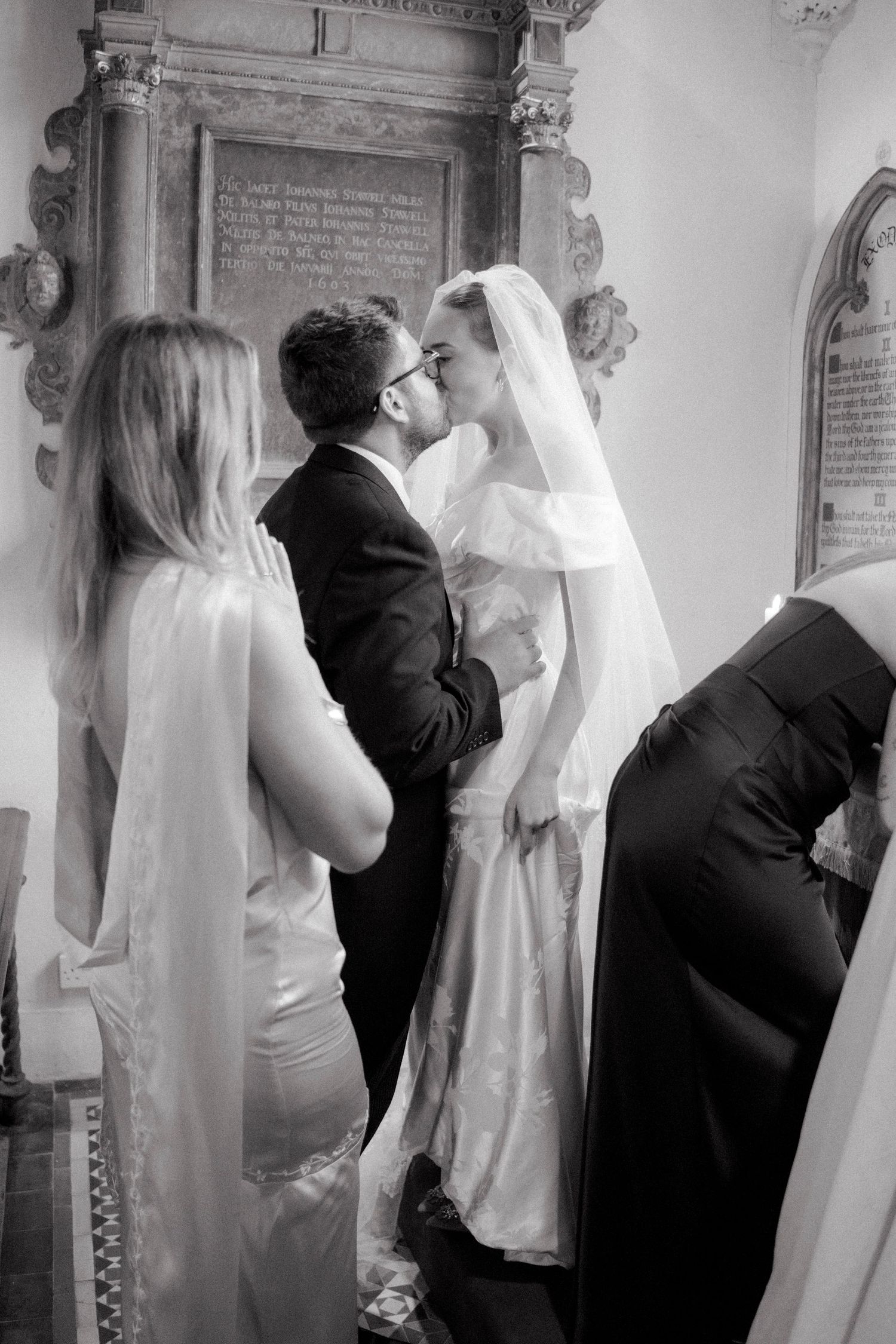Bride and groom share first kiss at church altar in elegant black and white wedding ceremony photo.