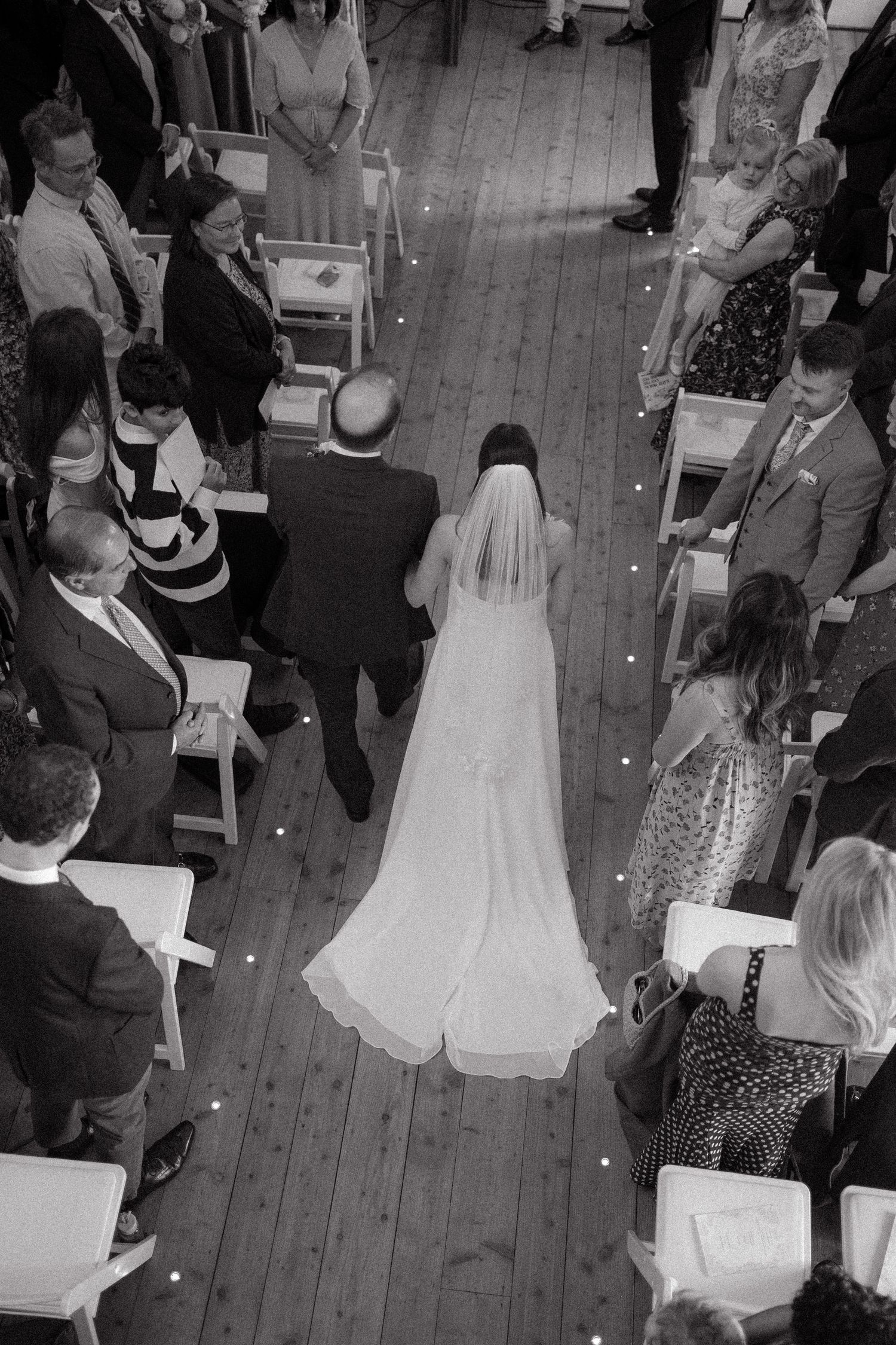 Black and white overhead view of wedding guests seated in rows during an indoor ceremony.
