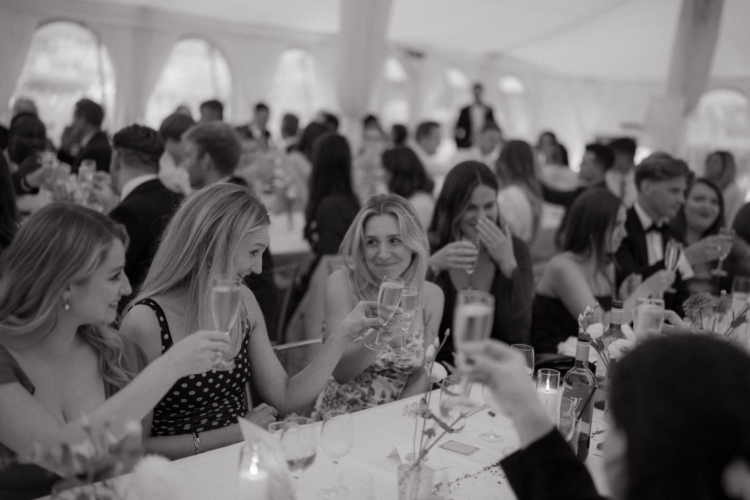 Black and white photo of wedding reception guests enjoying conversation at decorated dining tables.