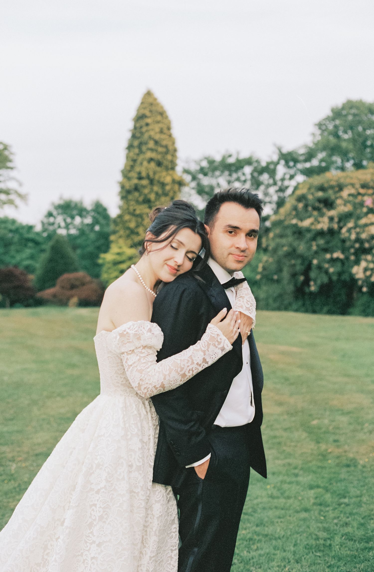 Romantic garden wedding portrait with elegant white lace dress and black tuxedo.