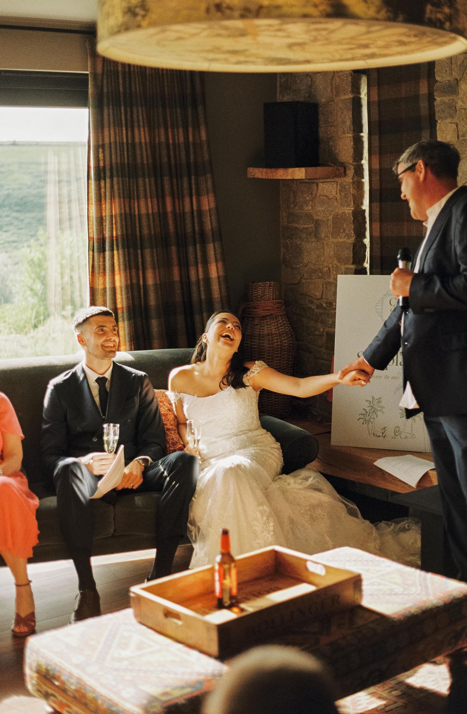 Wedding party relaxing and sharing drinks in a cozy indoor setting with wooden furnishings.