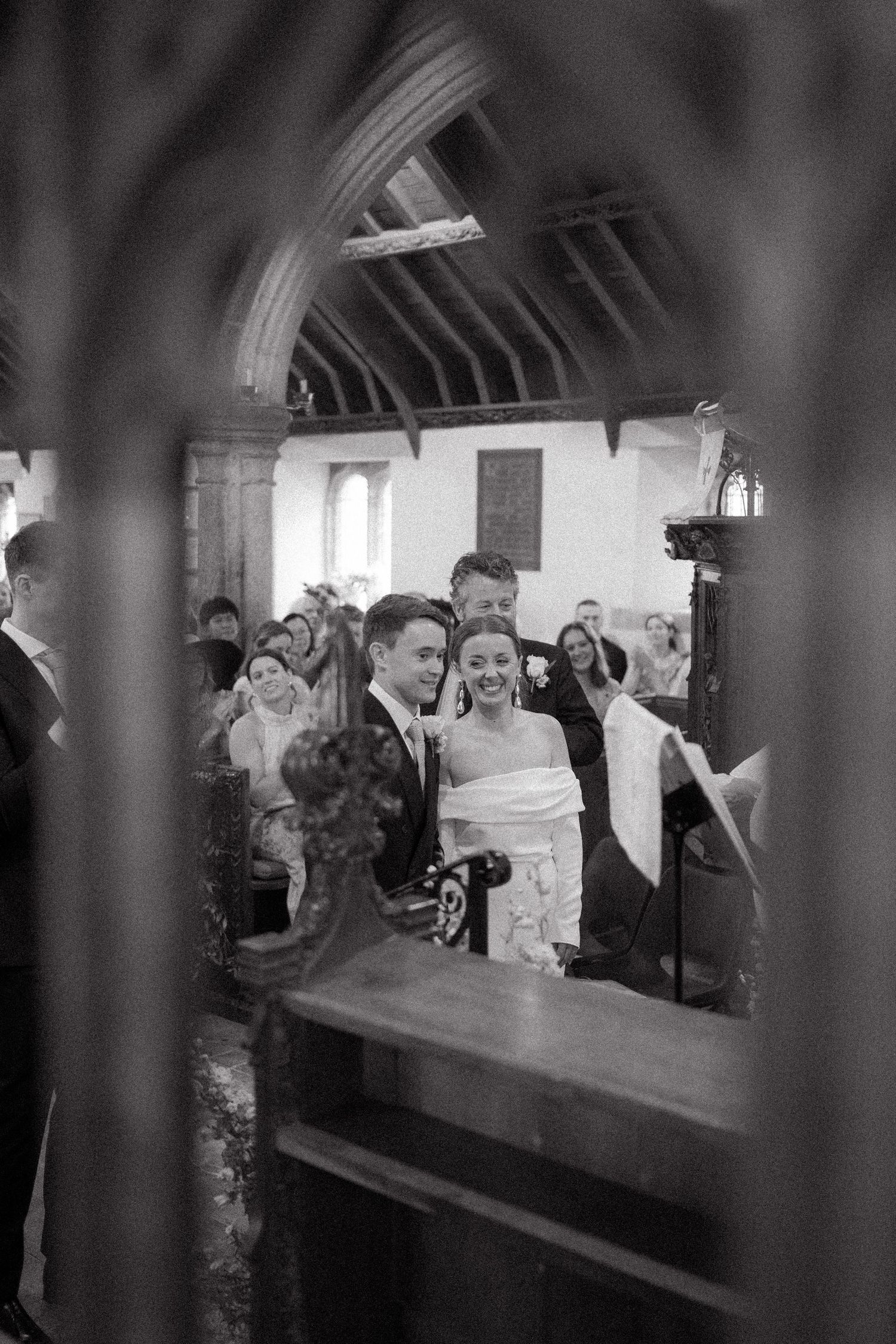 Black and white wedding ceremony photo captured through an archway in a traditional church setting.