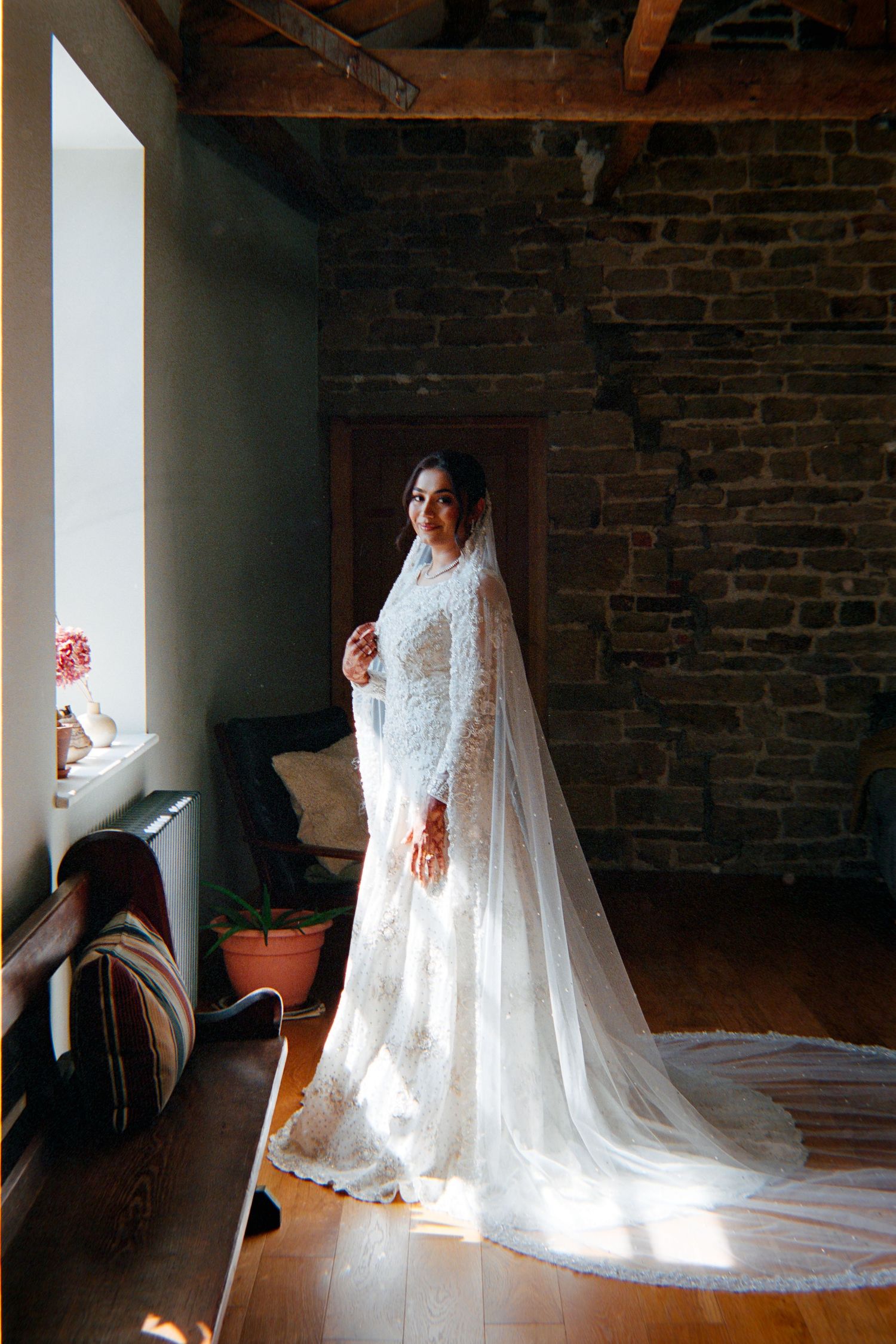 A sequence of photos showing a wedding dress with a long flowing veil in natural window light against exposed brick walls.
