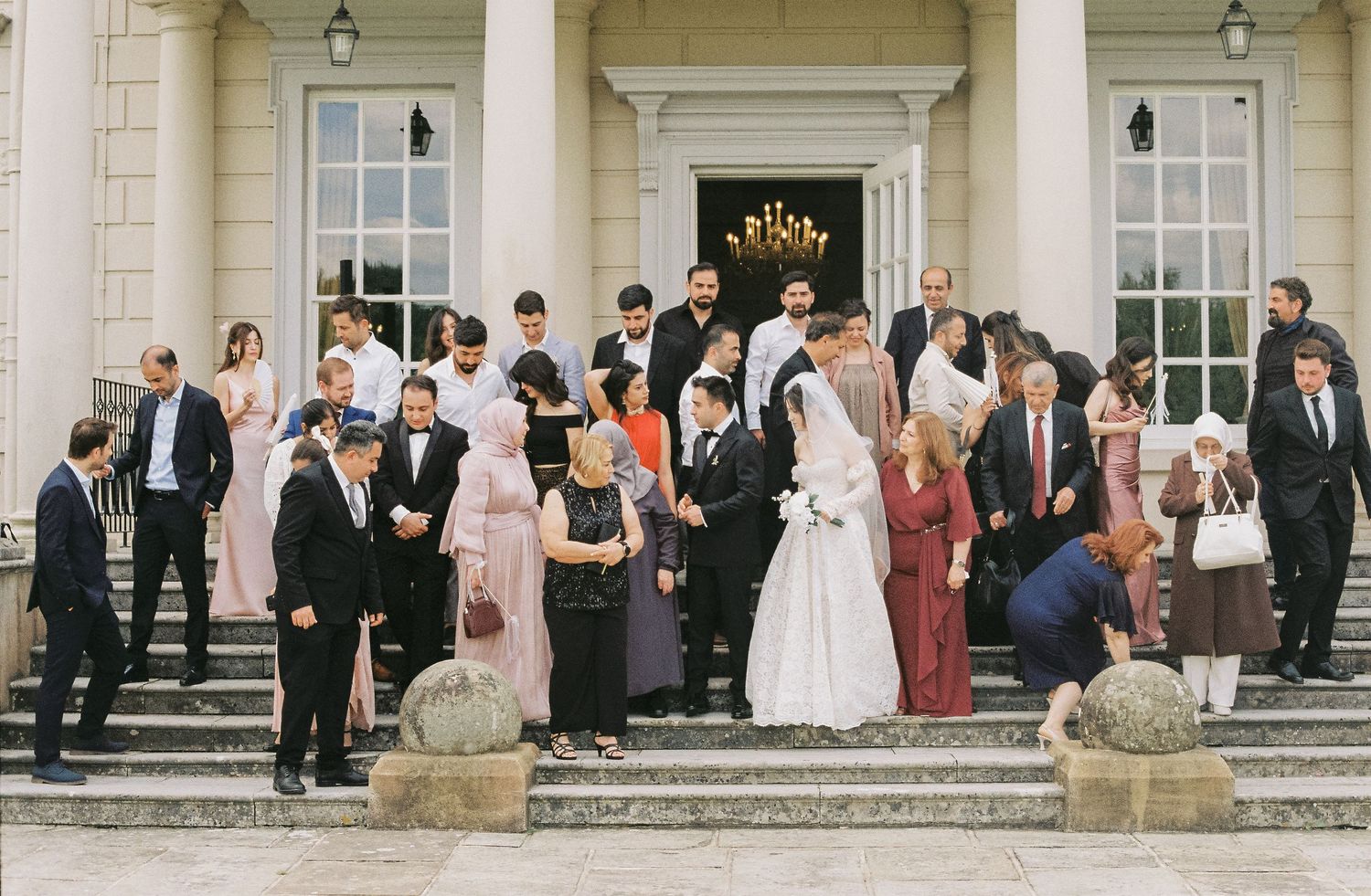 Wedding party and guests gathered on grand steps of classical white building.