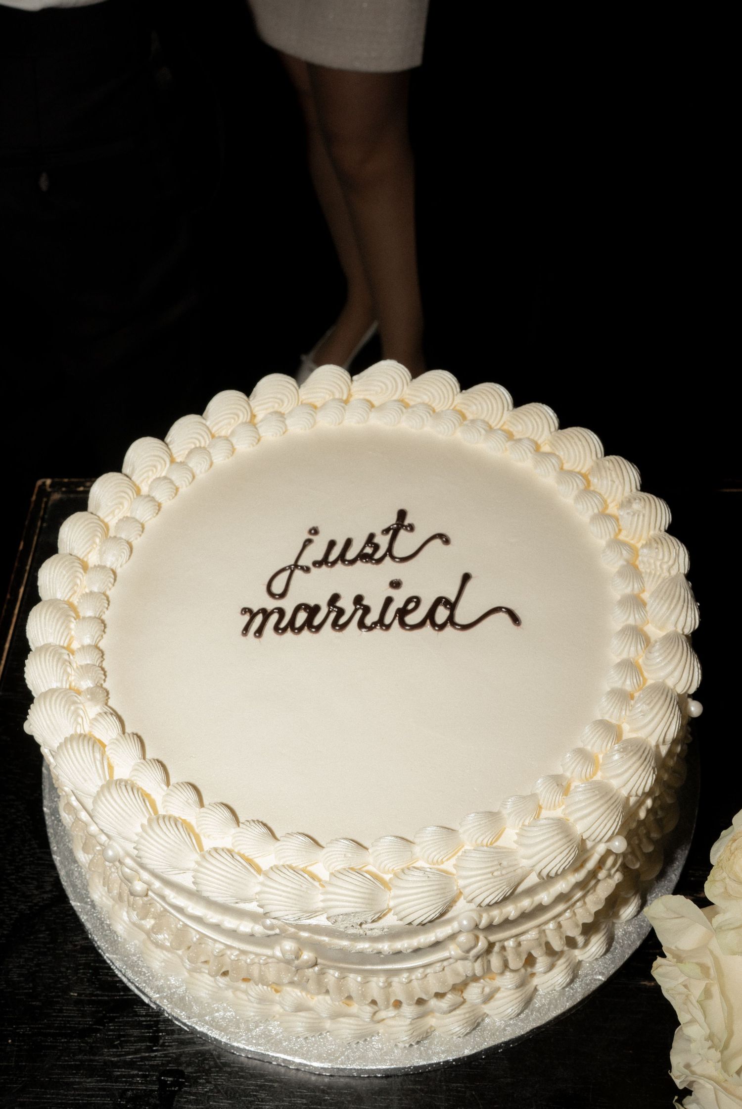 White wedding cake with pearl decorations and 'just married' text written in elegant script.