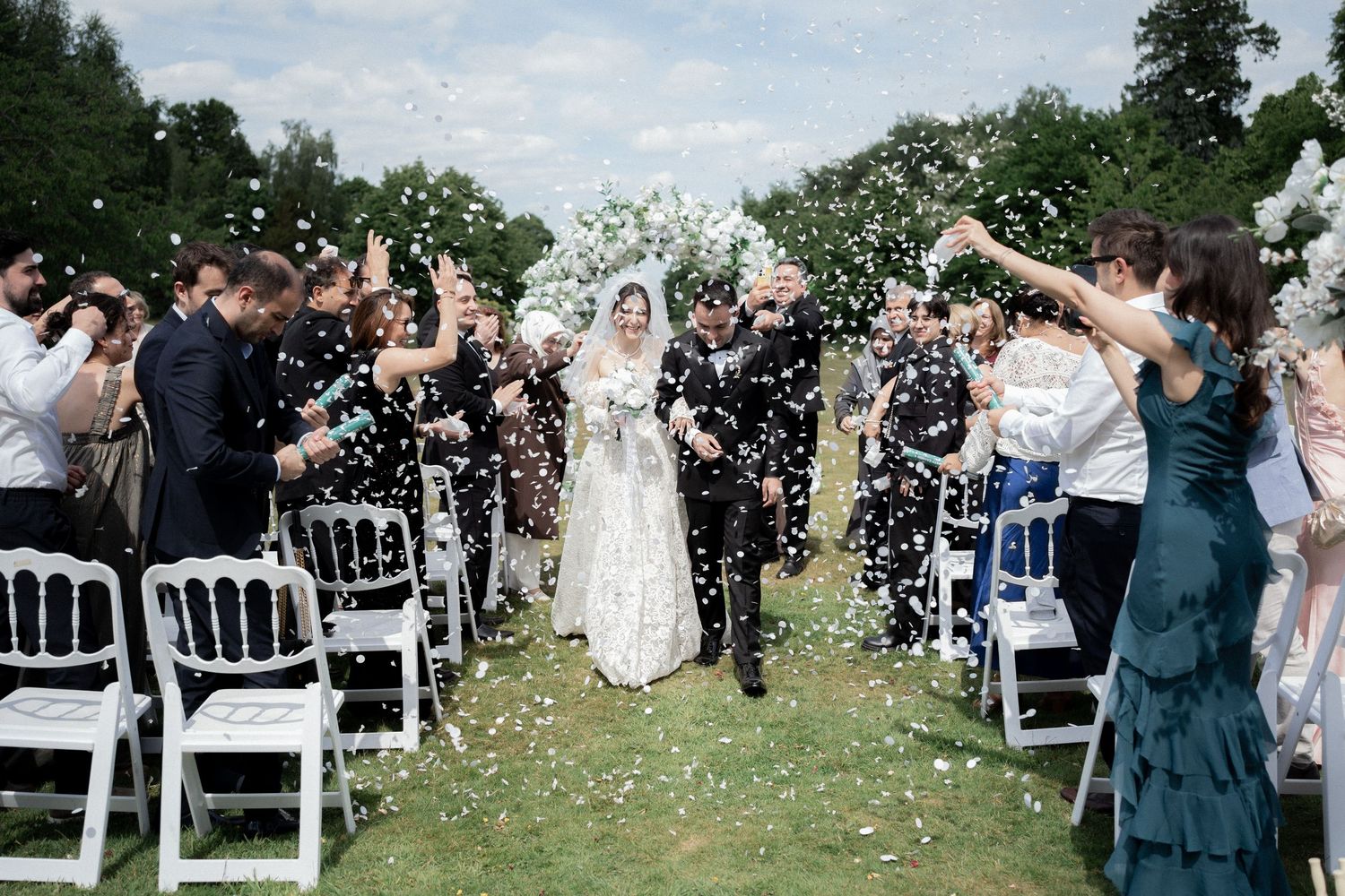 Wedding guests throw white confetti during an outdoor celebration.