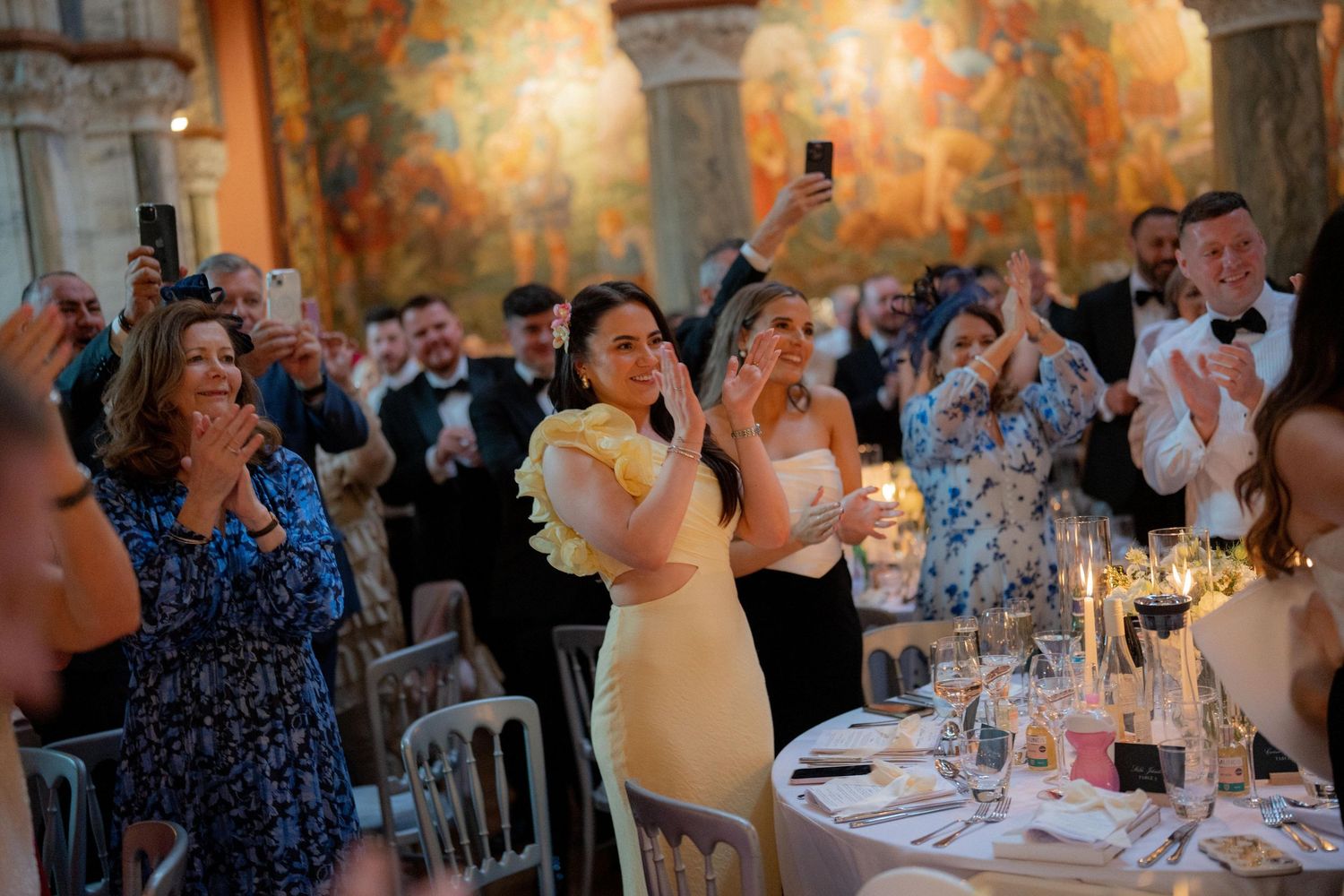 Wedding guests celebrate and take photos during an indoor reception with ornate wall murals.