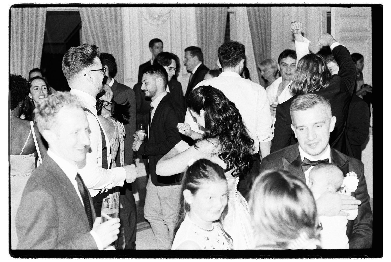 Black and white photo of elegantly dressed guests dancing and socializing at a formal event or prom.