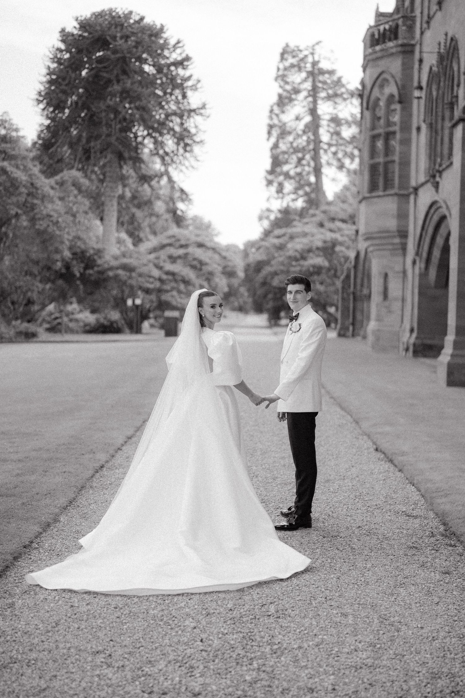 Black and white wedding photography on a gravel path beside a Gothic building.
