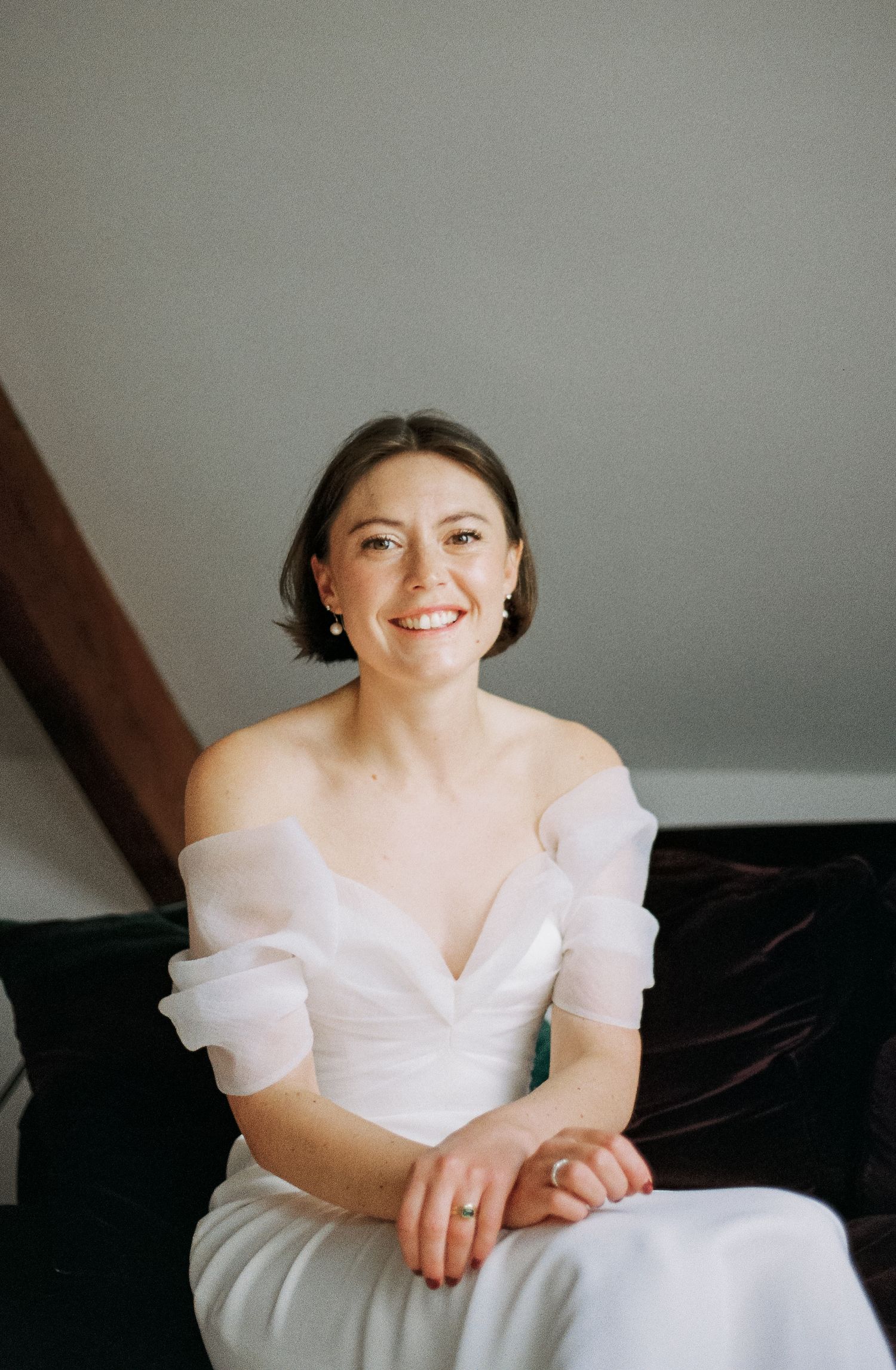 Bride in an off-shoulder white wedding dress poses against a grey background.
