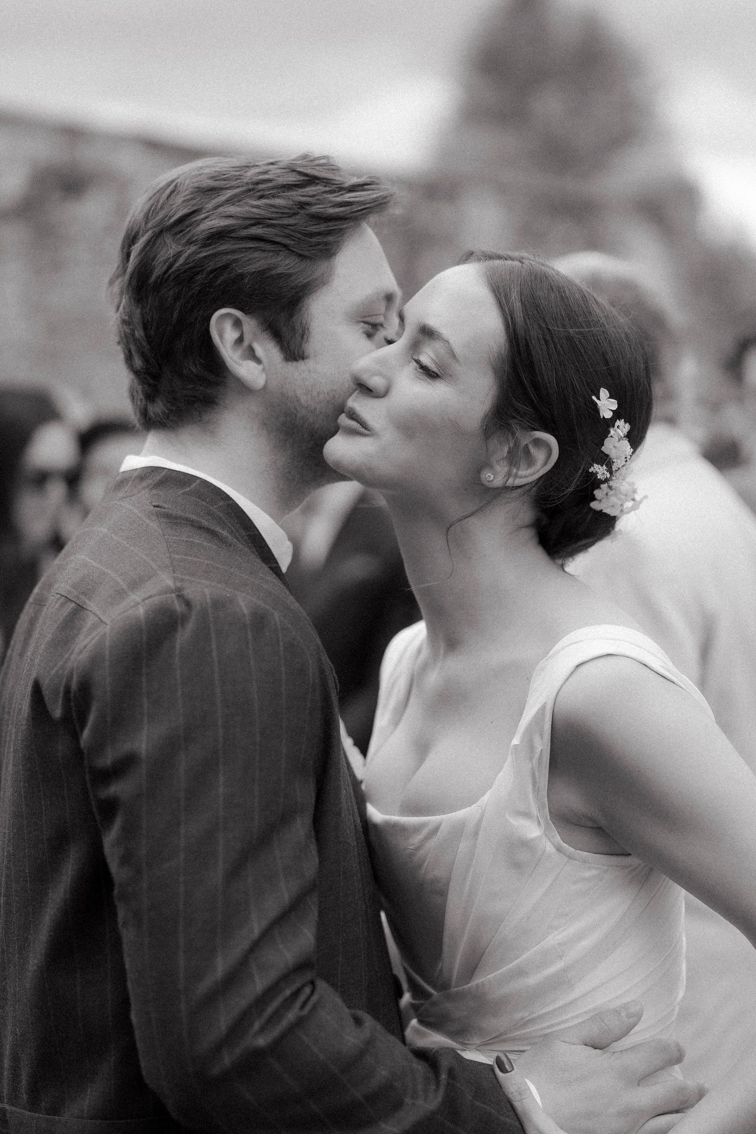 Black and white portrait of a bride with a floral hairpiece sharing a tender kiss on the cheek with the groom in a pinstripe suit.