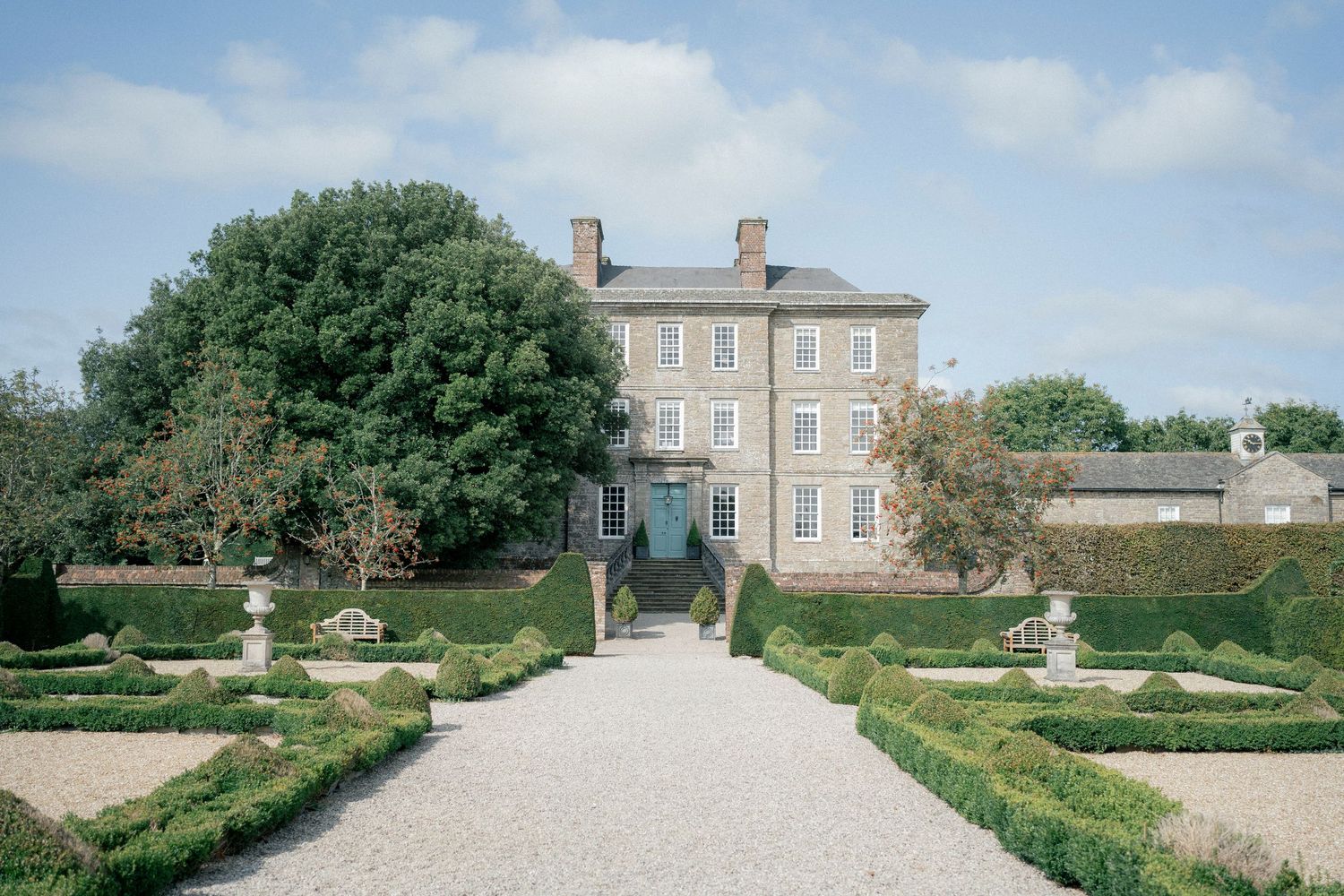 Georgian country house with formal box hedge parterre garden and gravel path leading to teal front door.