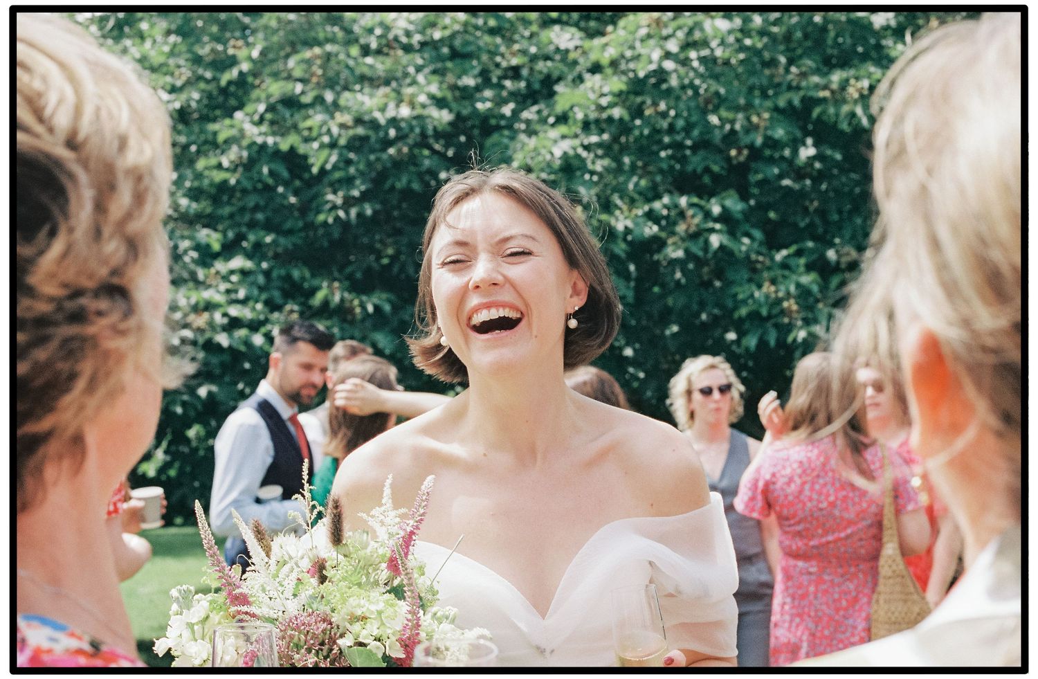 A group of people celebrating outdoors in a garden setting with joyful expressions and laughter.